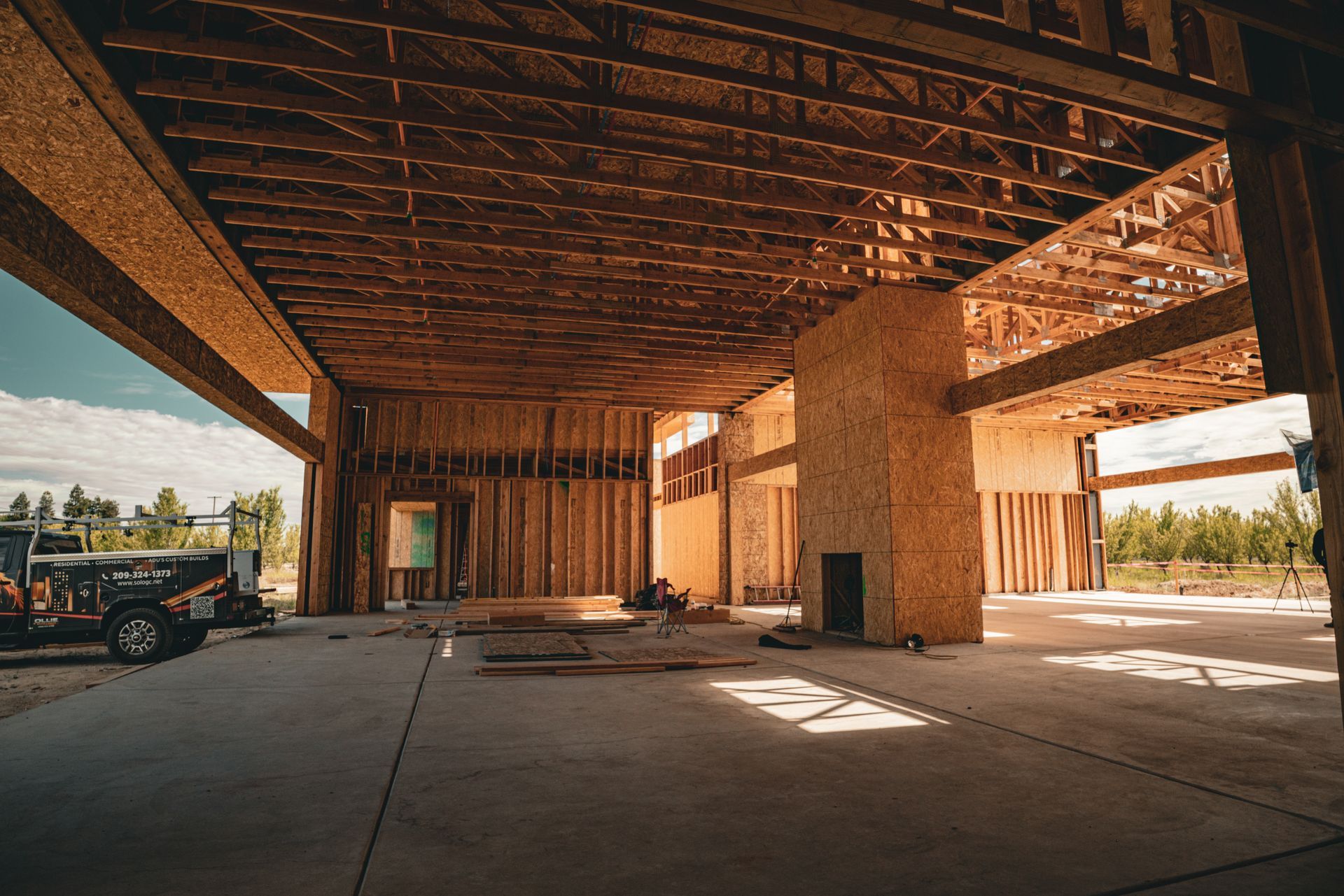 Partially built wooden interior of an open structure with concrete floor and sunlight streaming in