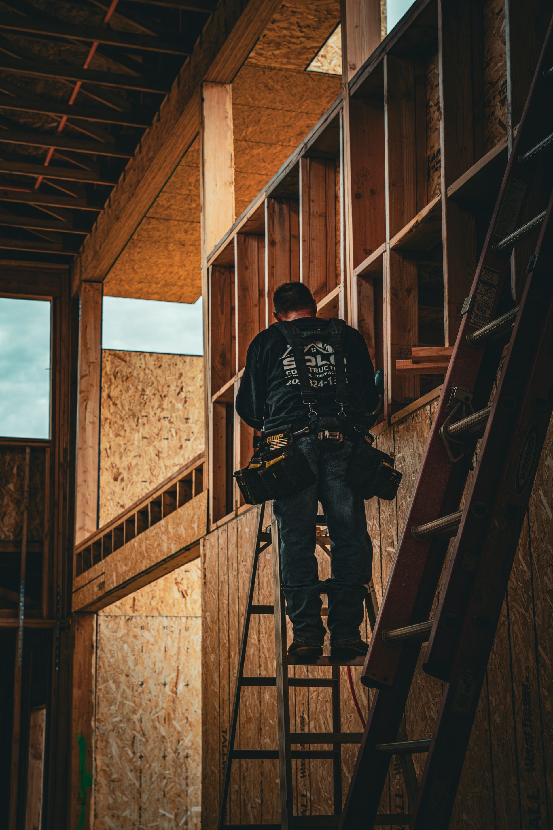 Person climbing a ladder inside a wooden building under construction