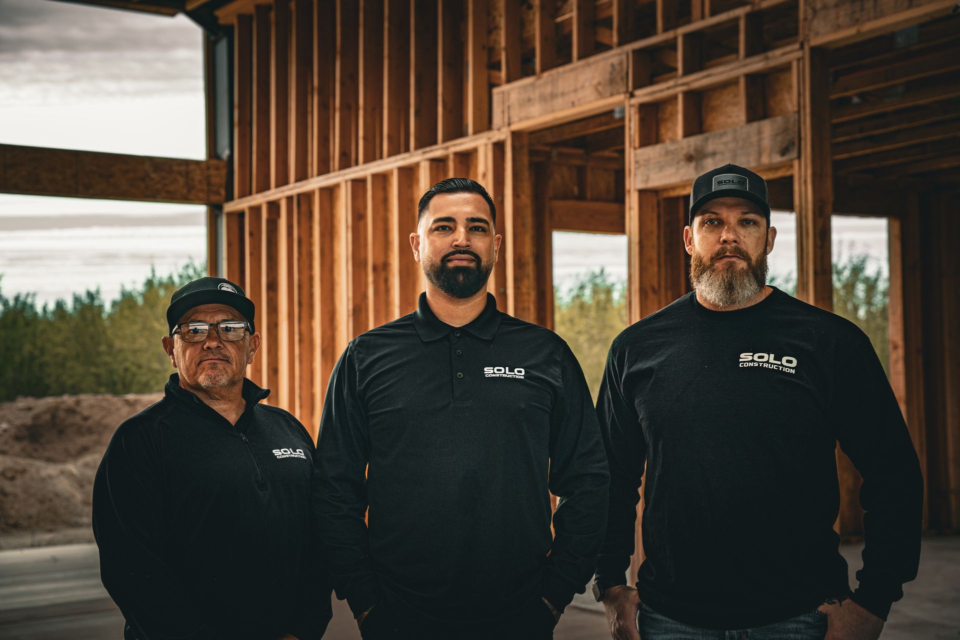 Three people in black shirts standing in front of a wood-framed building.