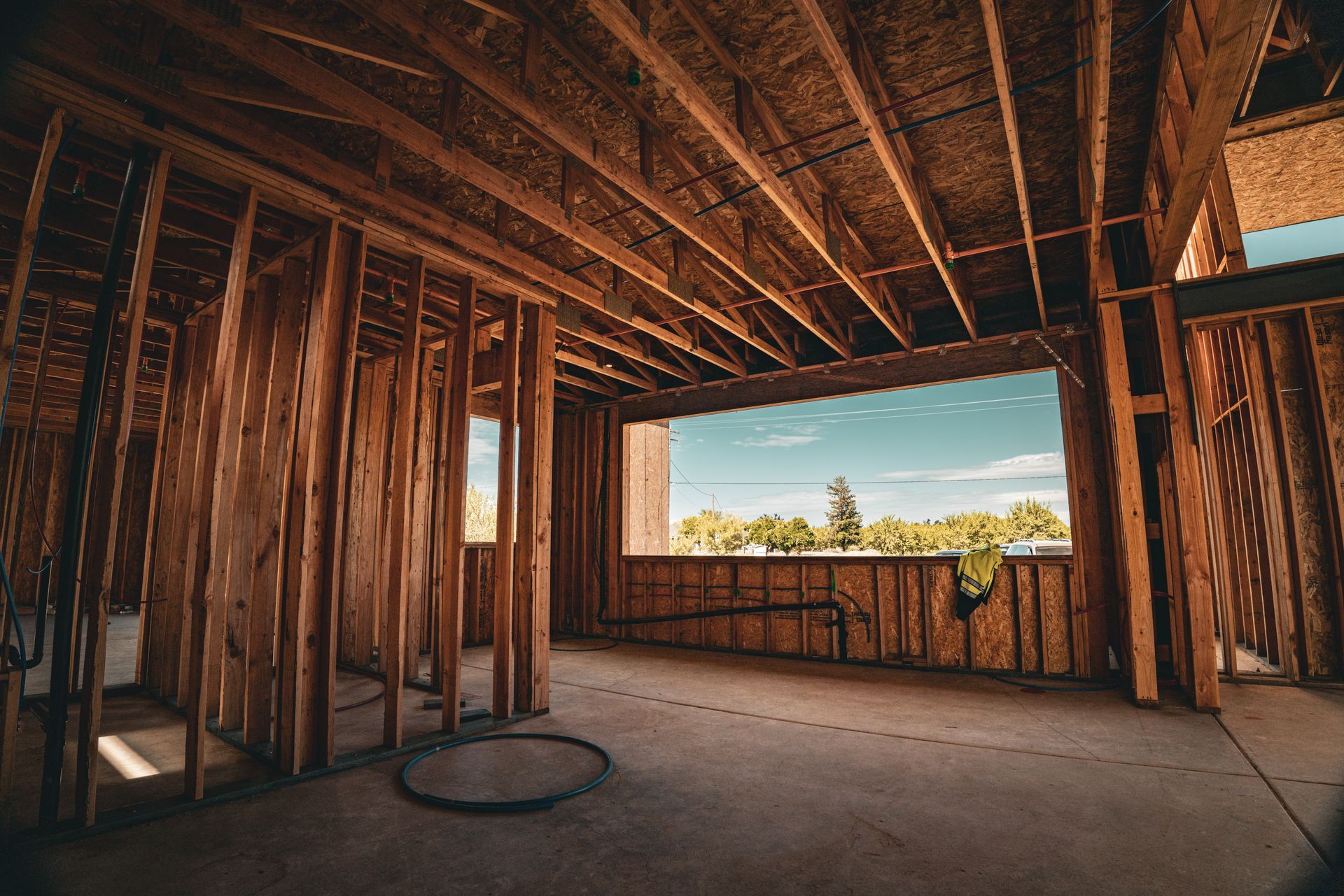 Unfinished wooden room with exposed beams and a large open window framing trees and sky.