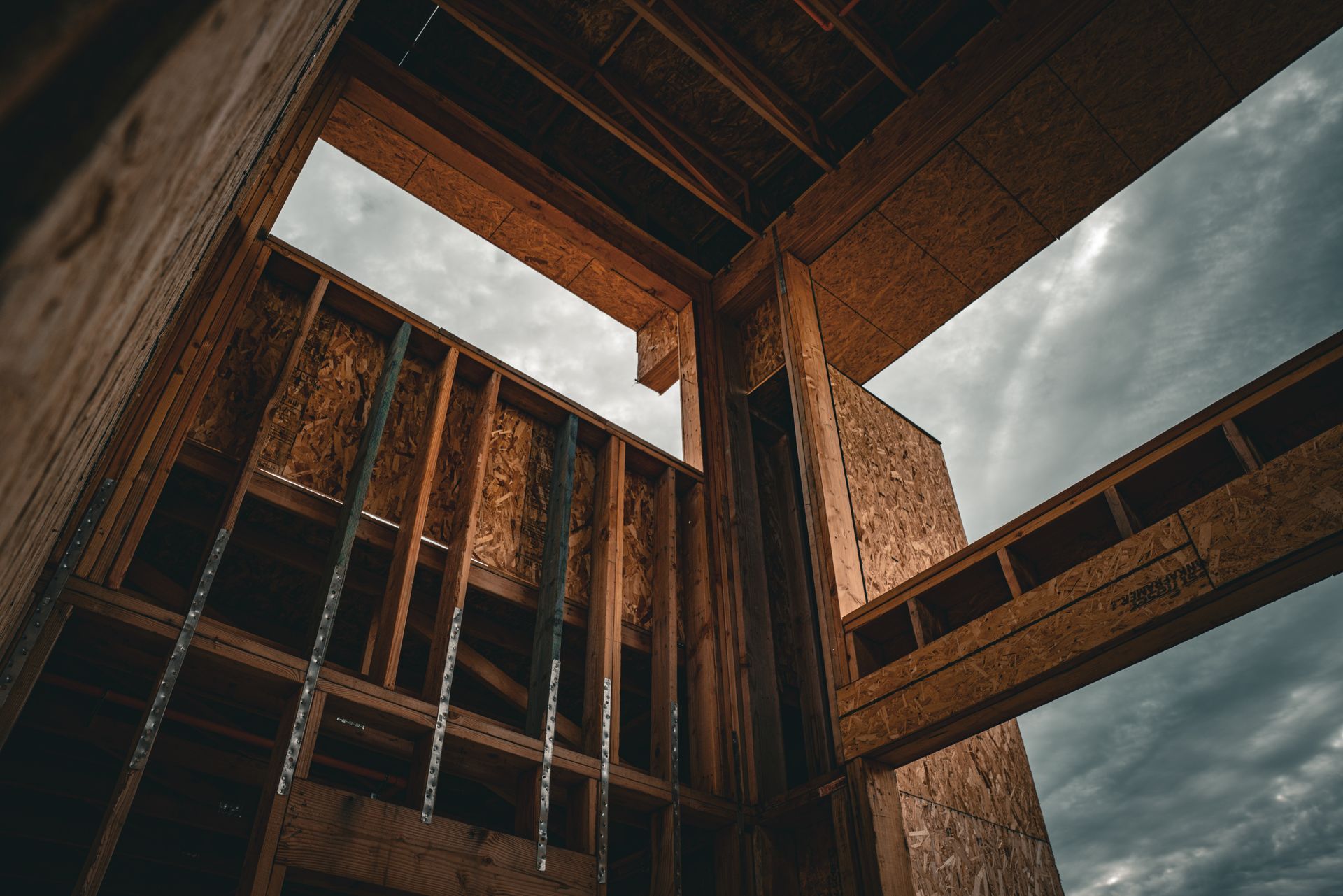 Low-angle view of an unfinished building frame with wooden beams and open skylights against a cloudy sky