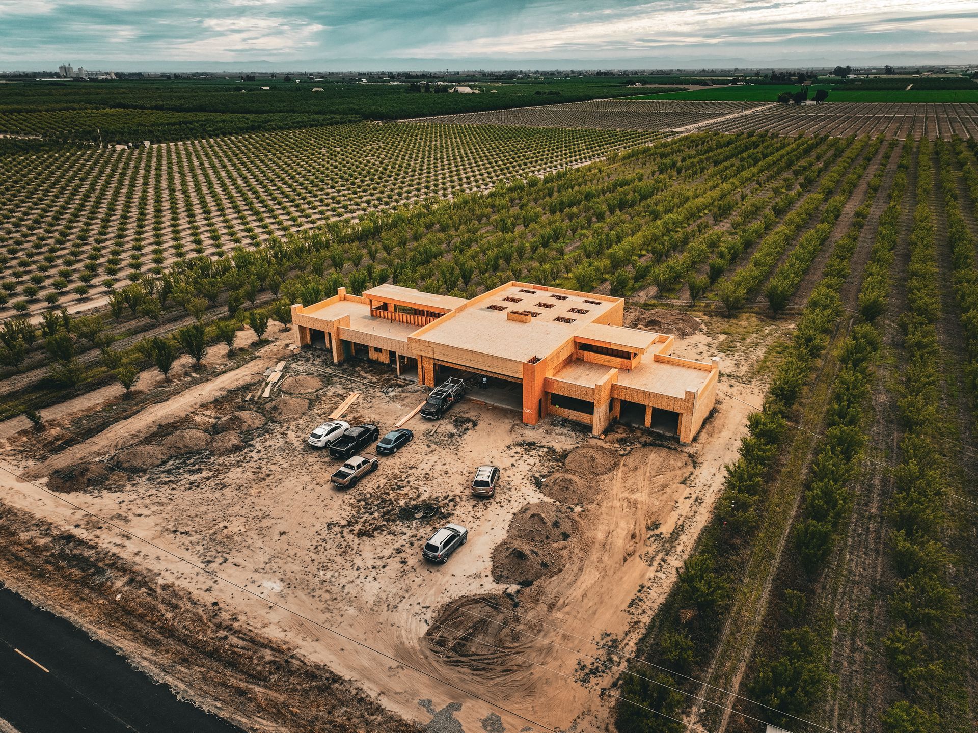 Aerial view of a large tan house under construction amid rows of green crops.