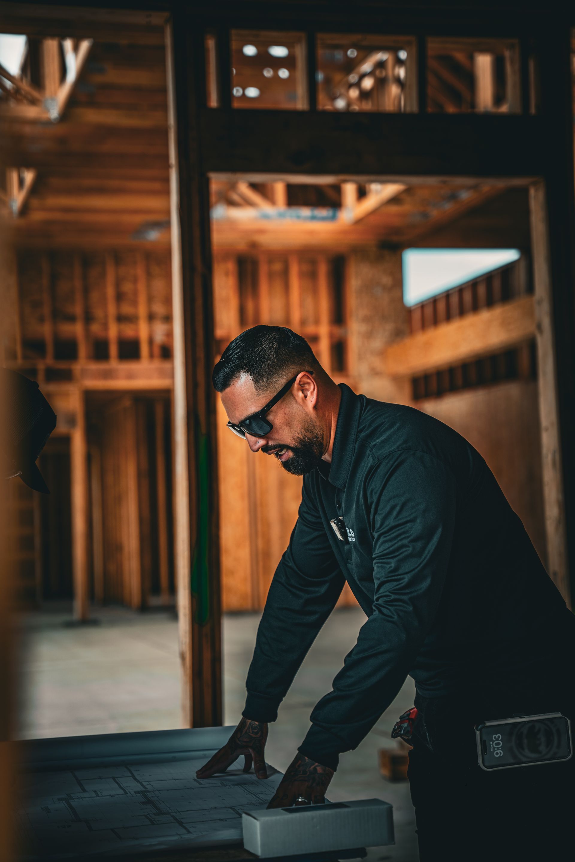 Man in dark clothing measuring wood inside an unfinished house frame