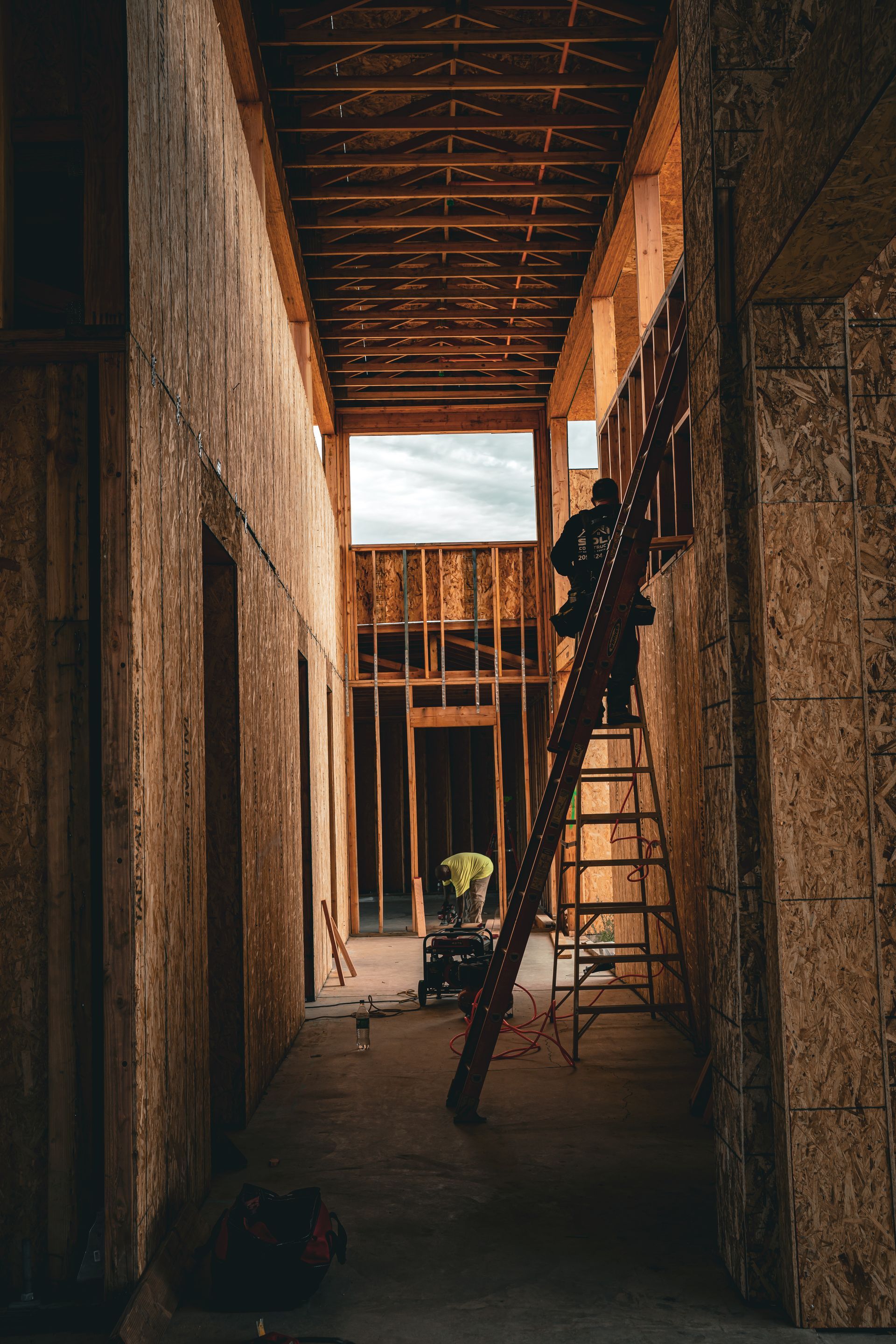 Narrow unfinished hallway with wooden framing, ladder, and construction materials inside a building site