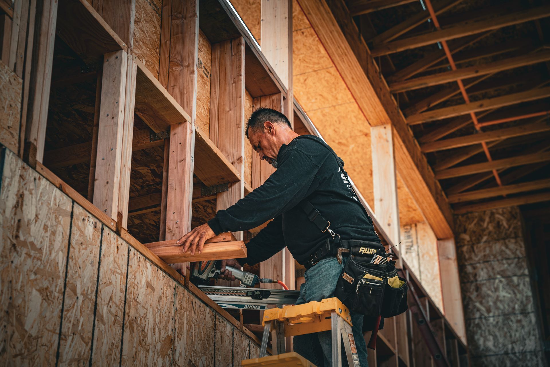 Worker using a power tool to cut framing wood inside an unfinished house
