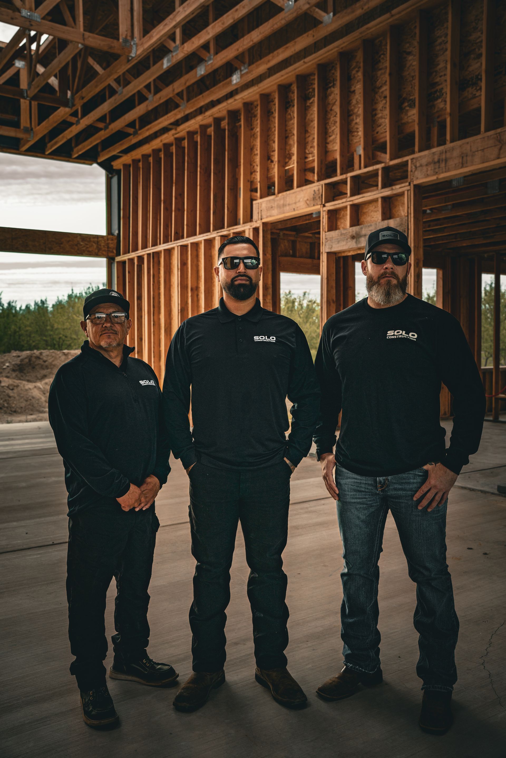Three people in black shirts and caps standing inside a partially built wooden structure.