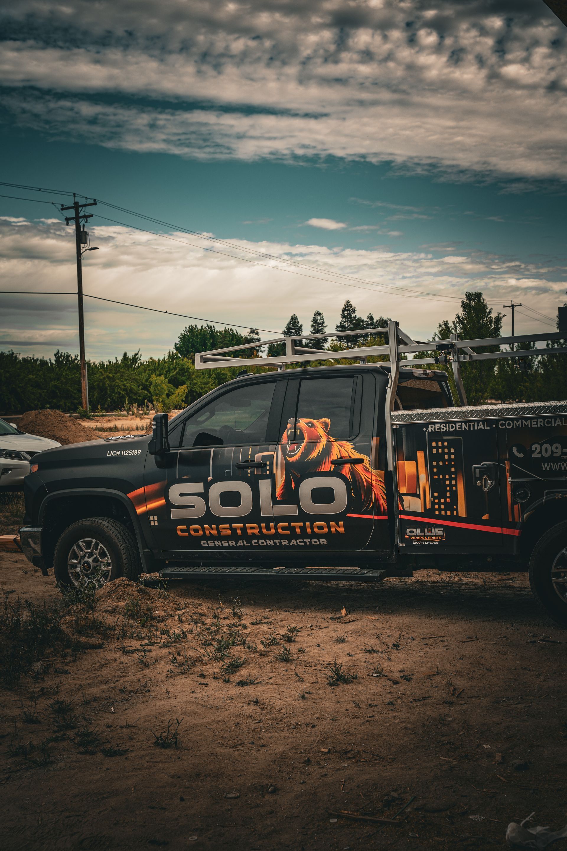 Black pickup truck with SOLO Tree Service branding parked on a dirt road under a cloudy sky.