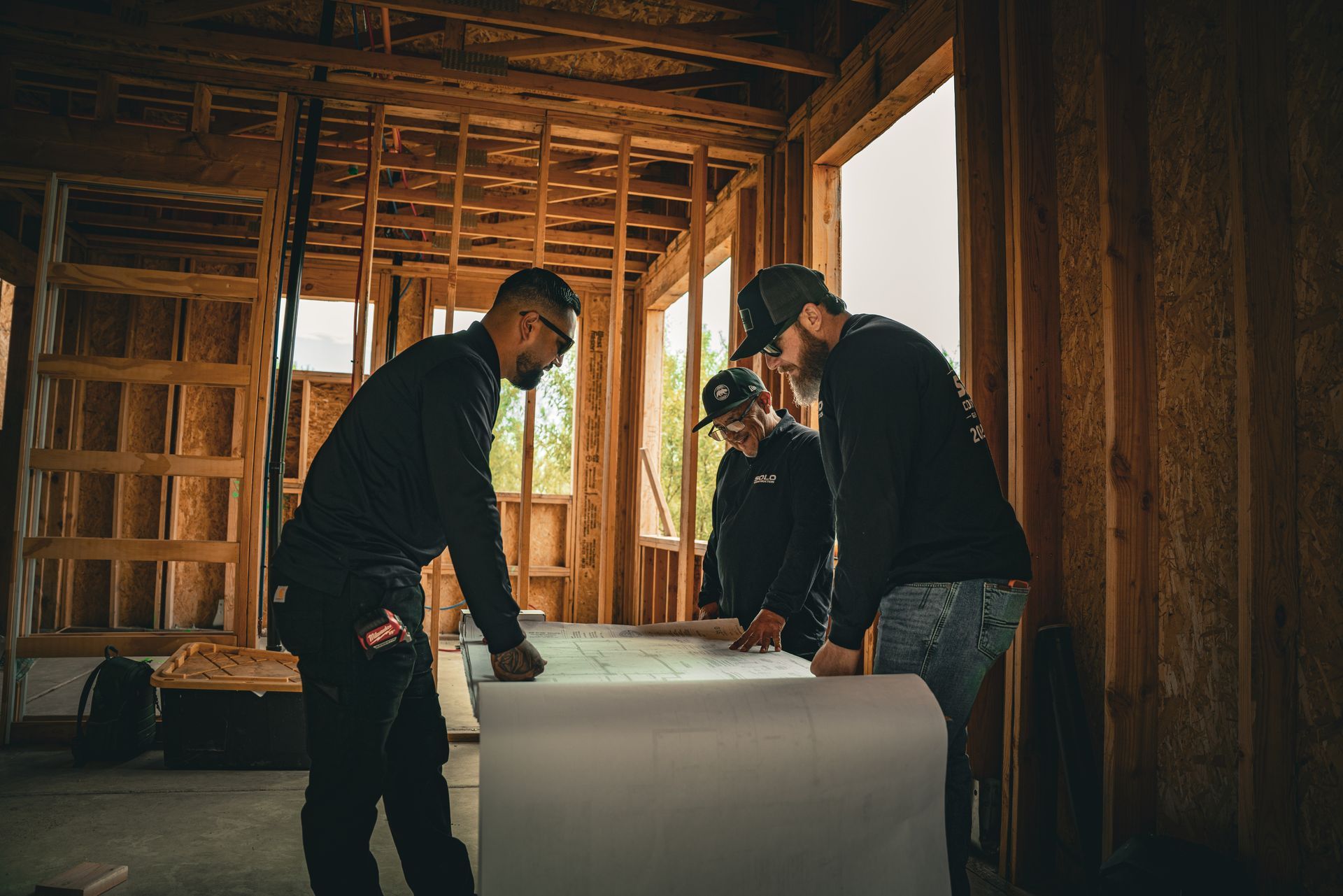 Workers reviewing blueprints inside a wooden-framed building under construction