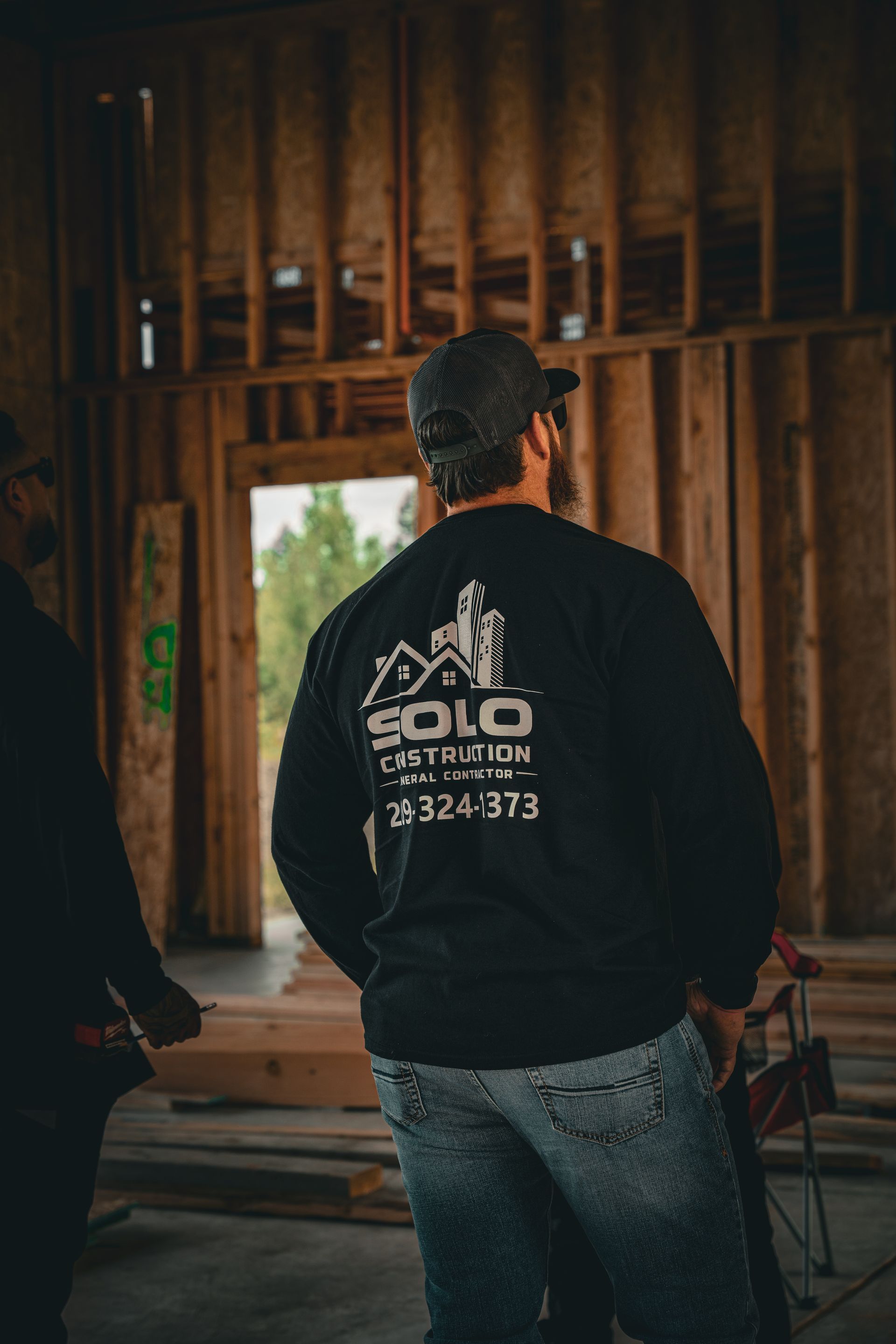 Person in black sweatshirt and jeans stands in a wooden-framed room, facing a window.