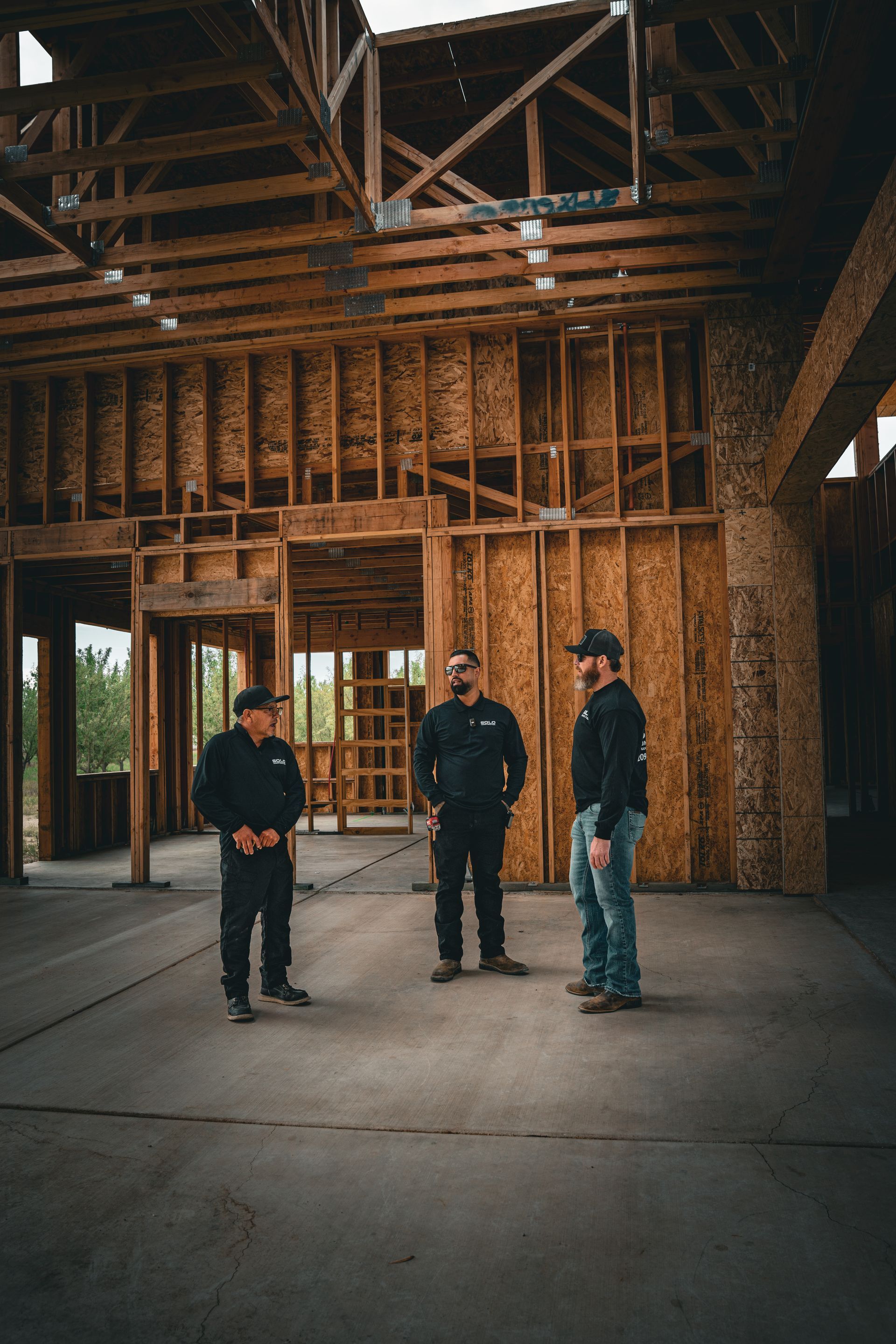 Three people standing inside a large unfinished wooden building with exposed framing and a concrete floor.