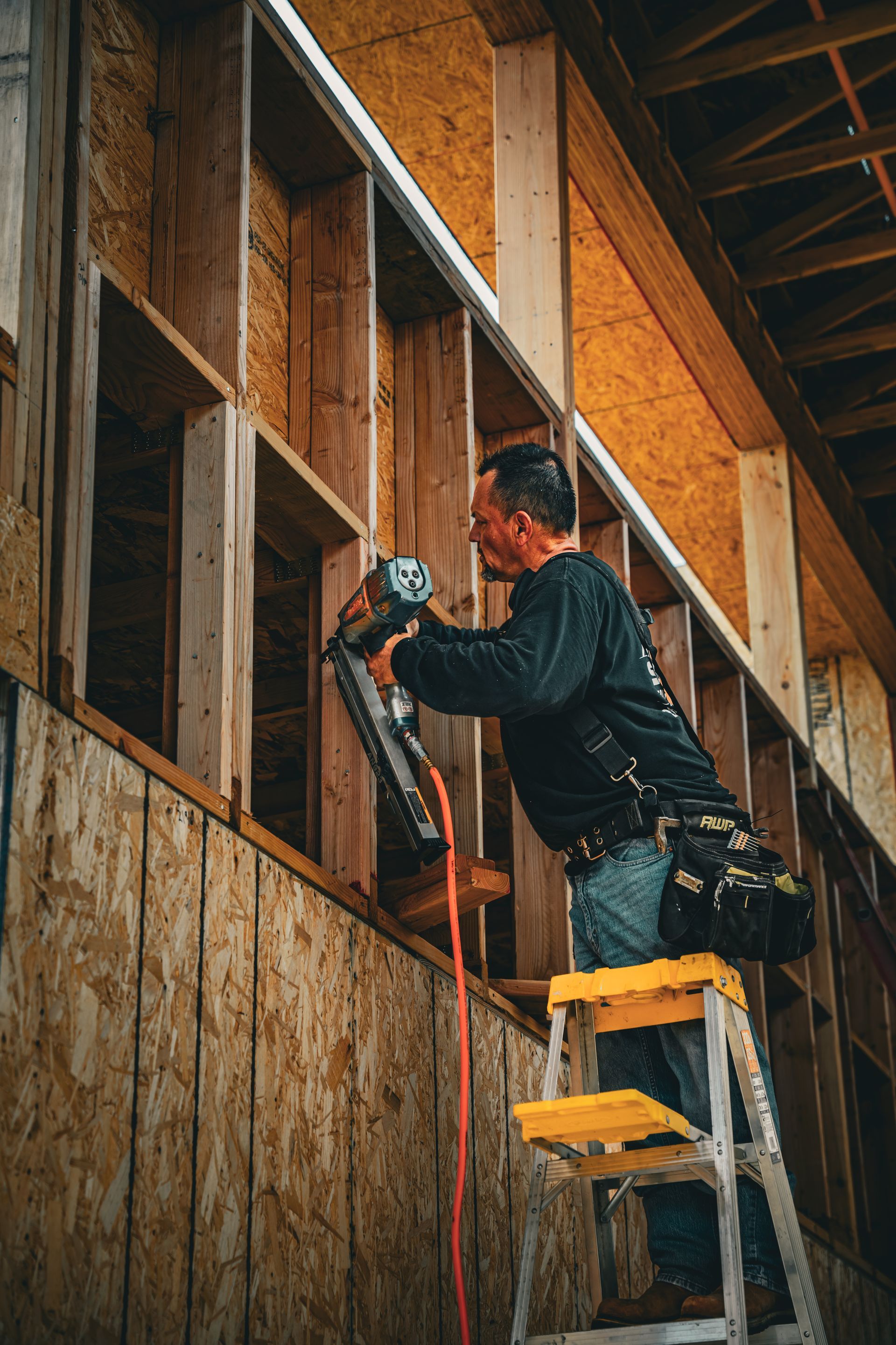Worker drilling into exposed wooden wall from a ladder in a construction site
