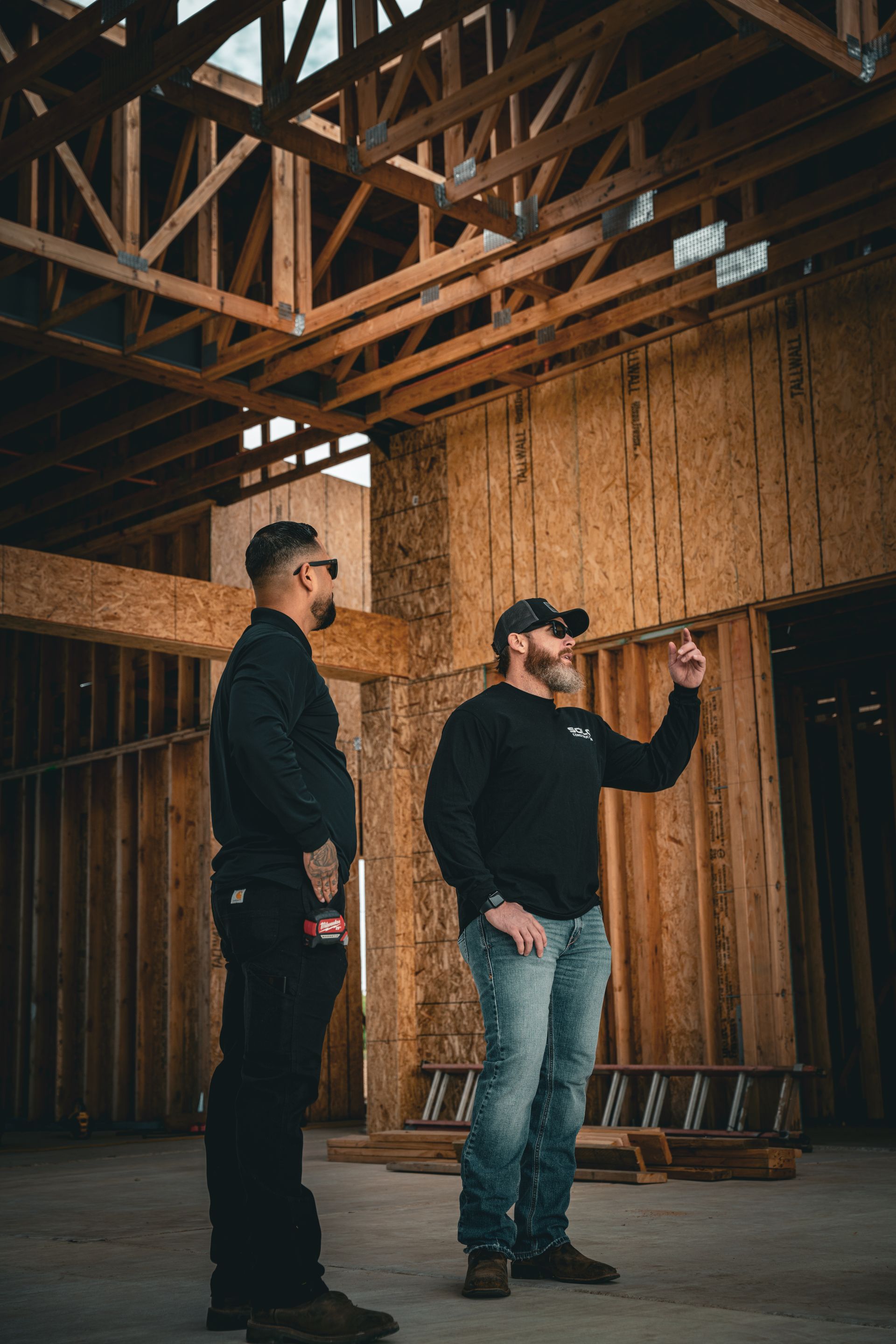 Two men standing in a wooden barn interior, one pointing ahead while the other watches.