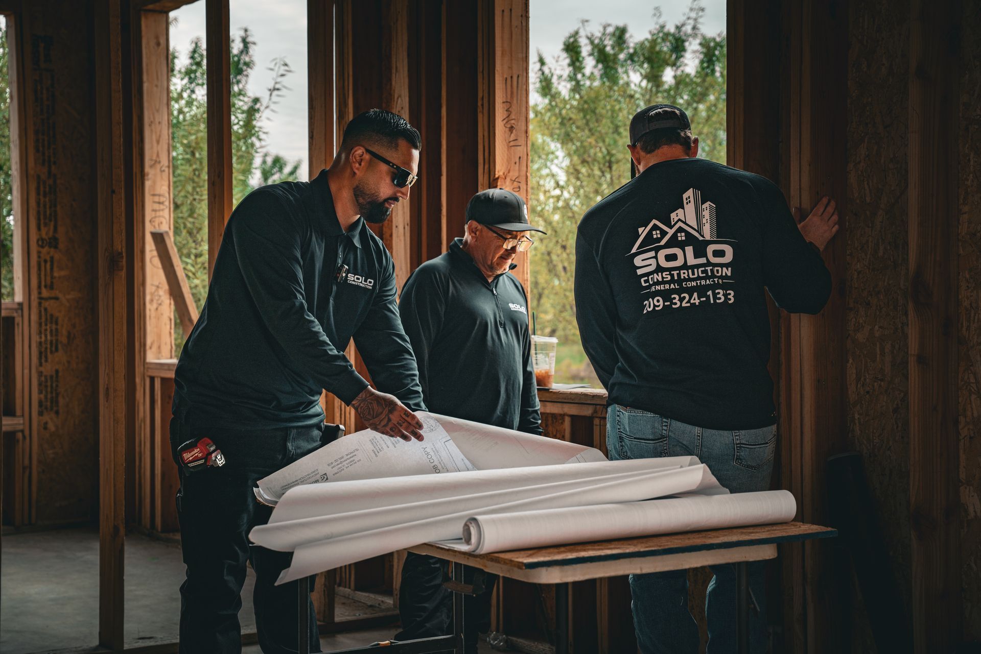 Three workers folding white insulation on a table inside a wooden-framed house under construction