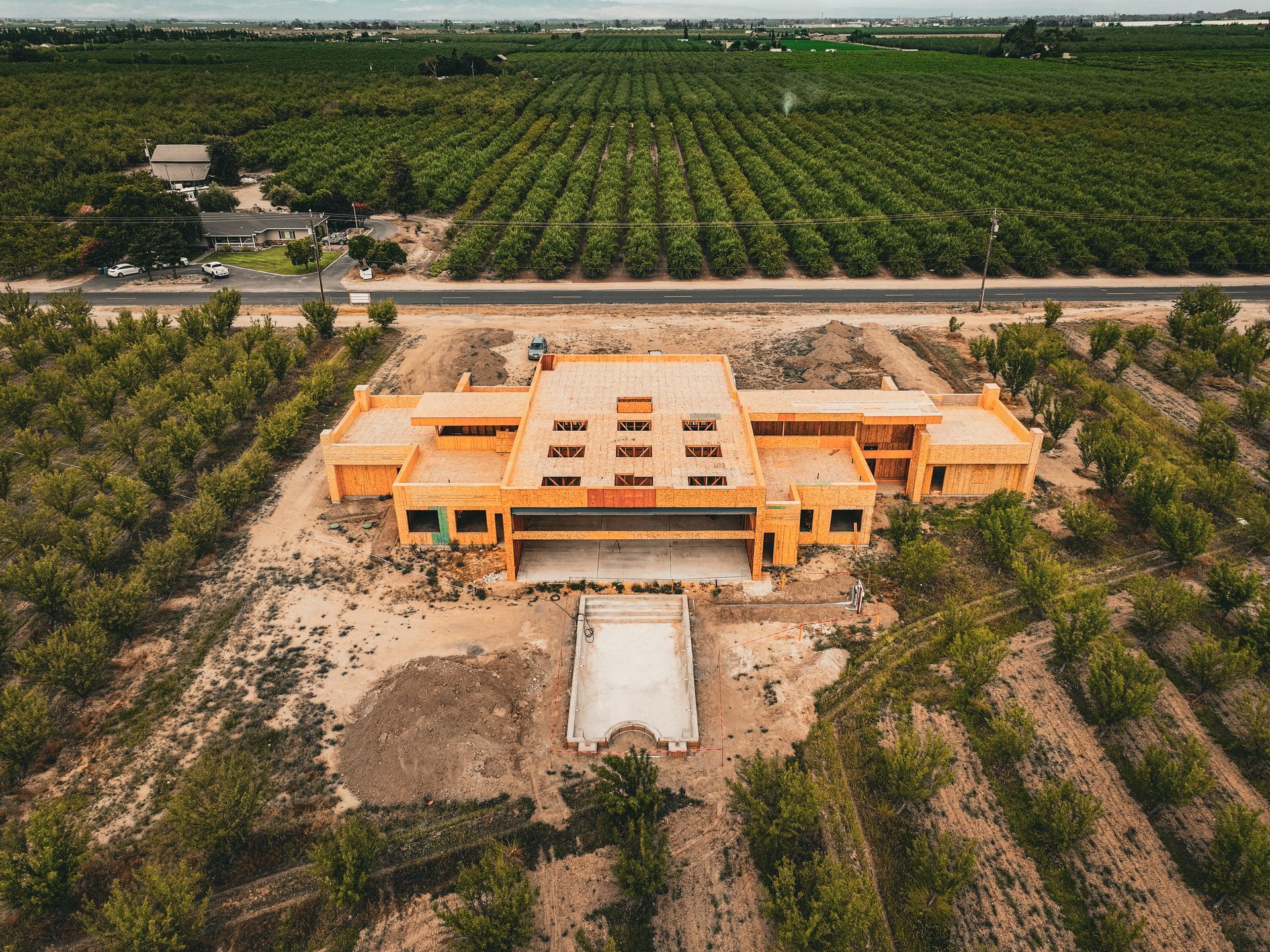 Aerial view of a large orange building amid farmland and trees, with a road in front.