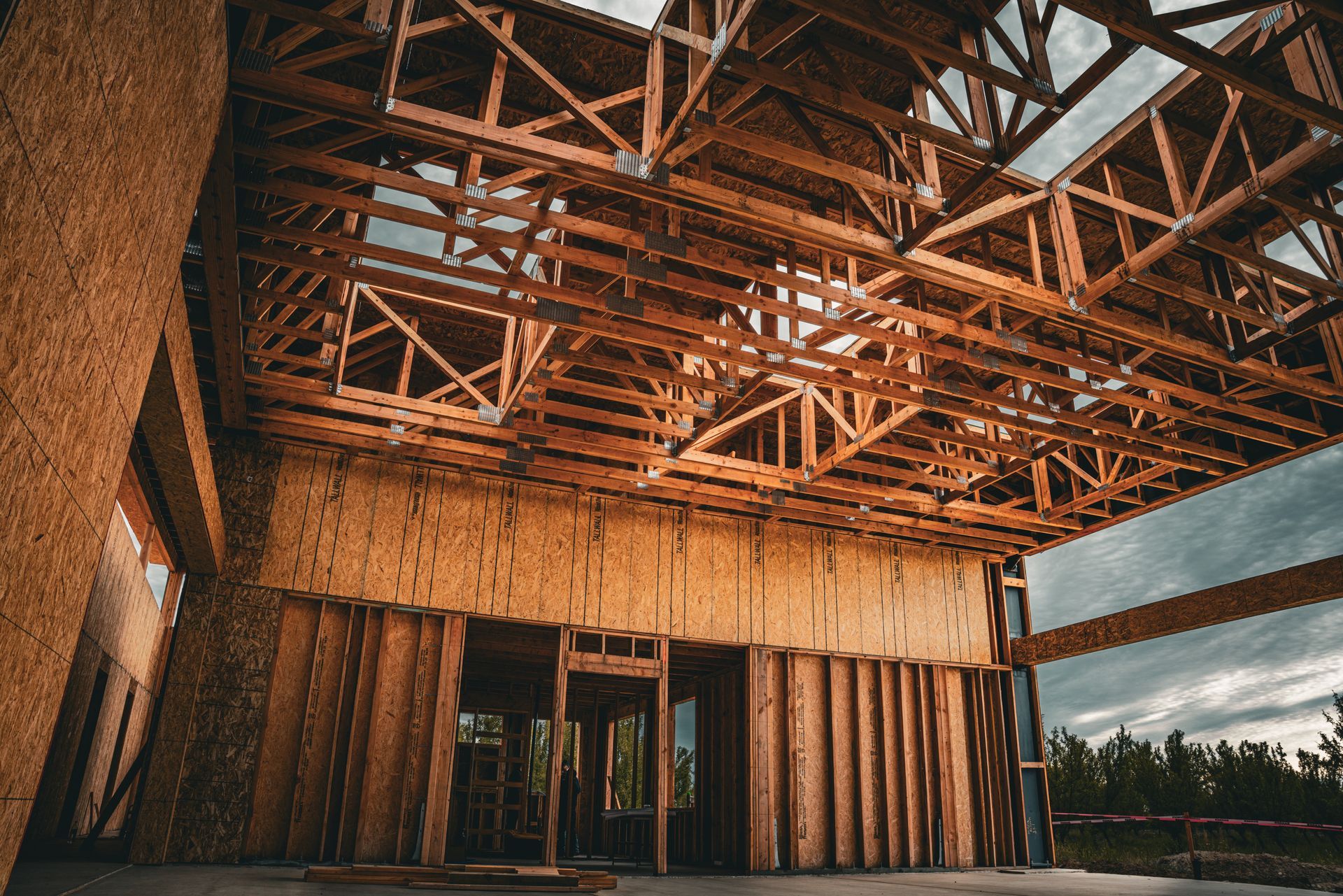 Unfinished wooden building interior with exposed roof trusses and framing, lit by warm sunlight.