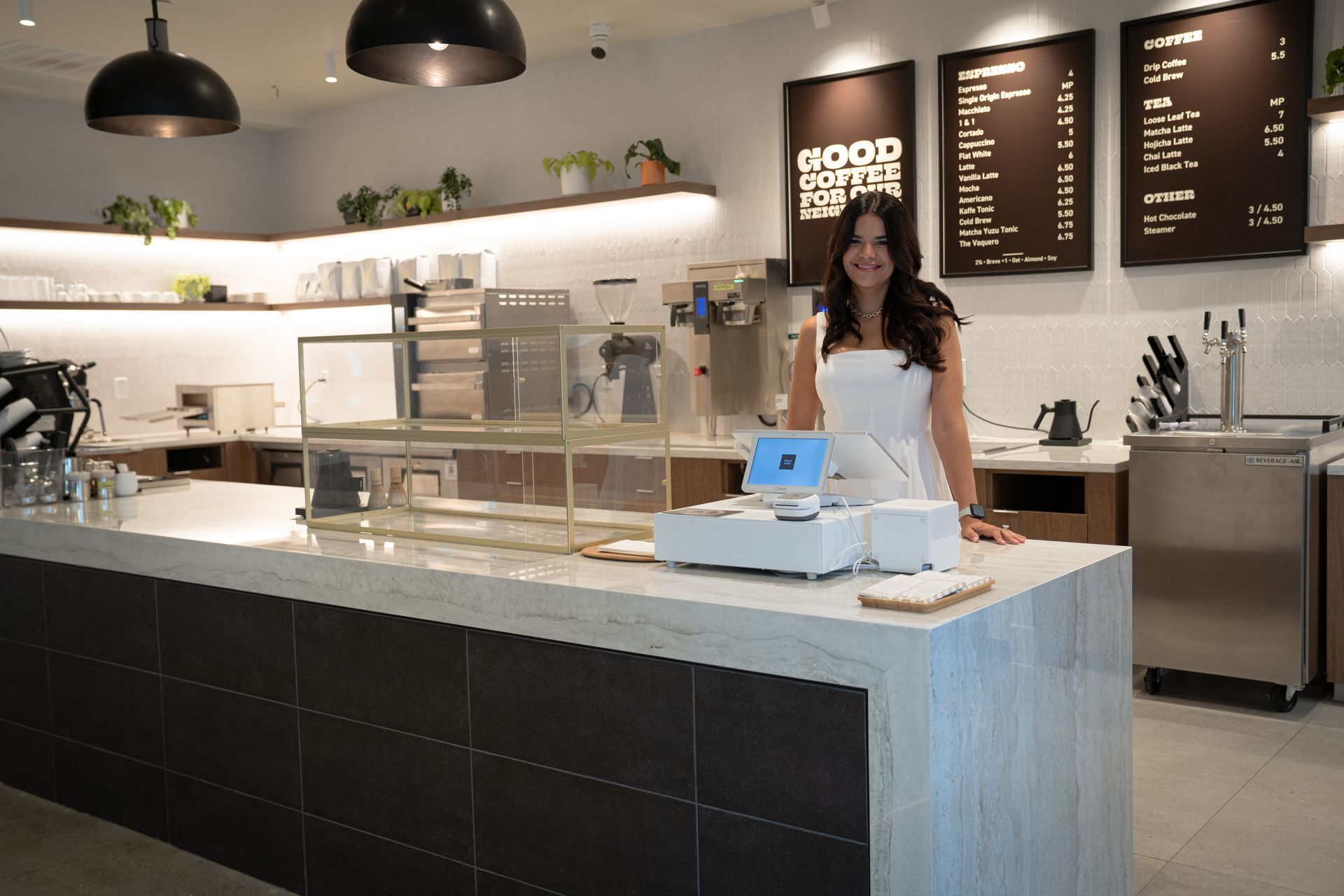 Café counter with a woman standing behind a register in a modern coffee shop