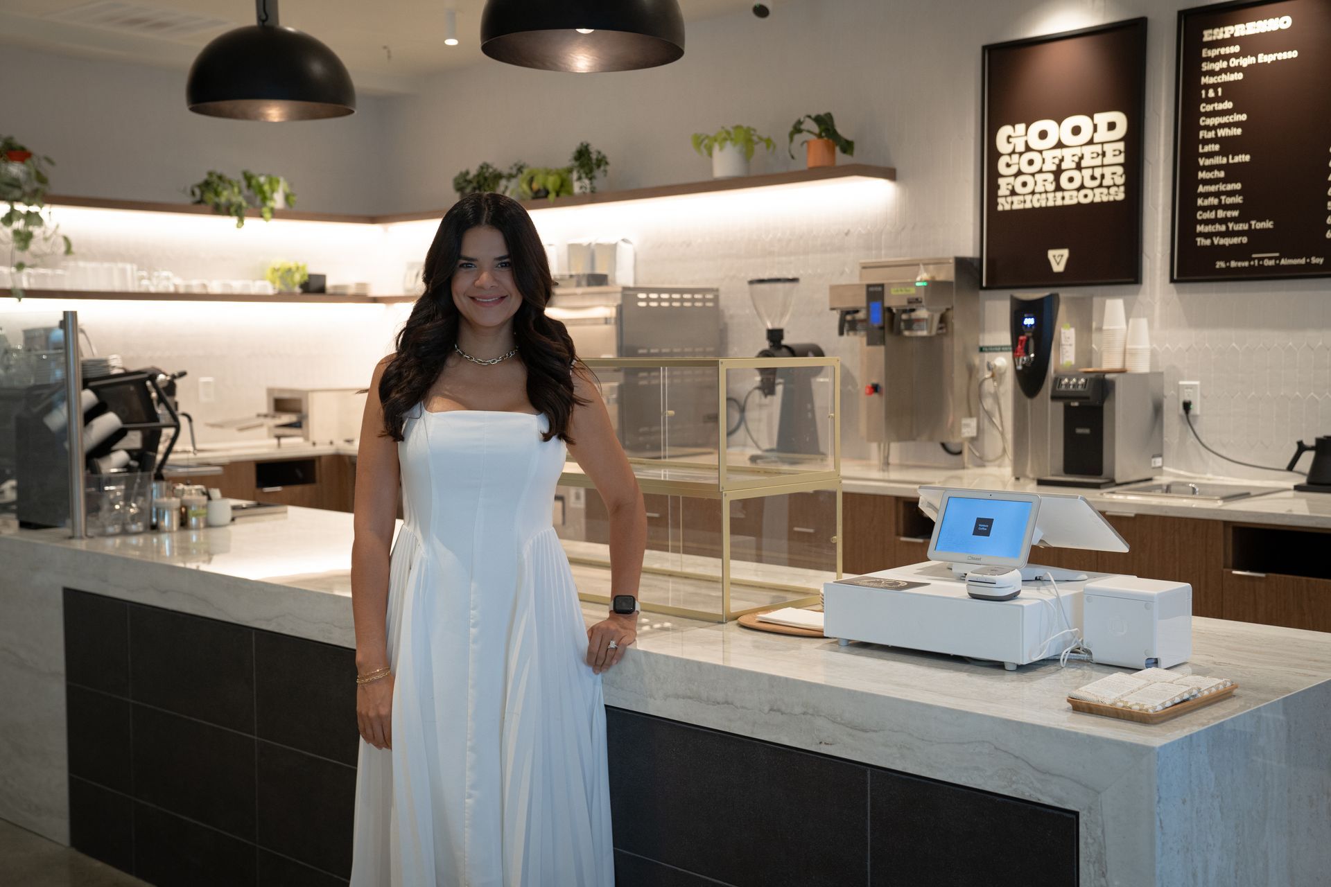 Woman in a white dress standing in a modern cafe beside the counter and pastry display
