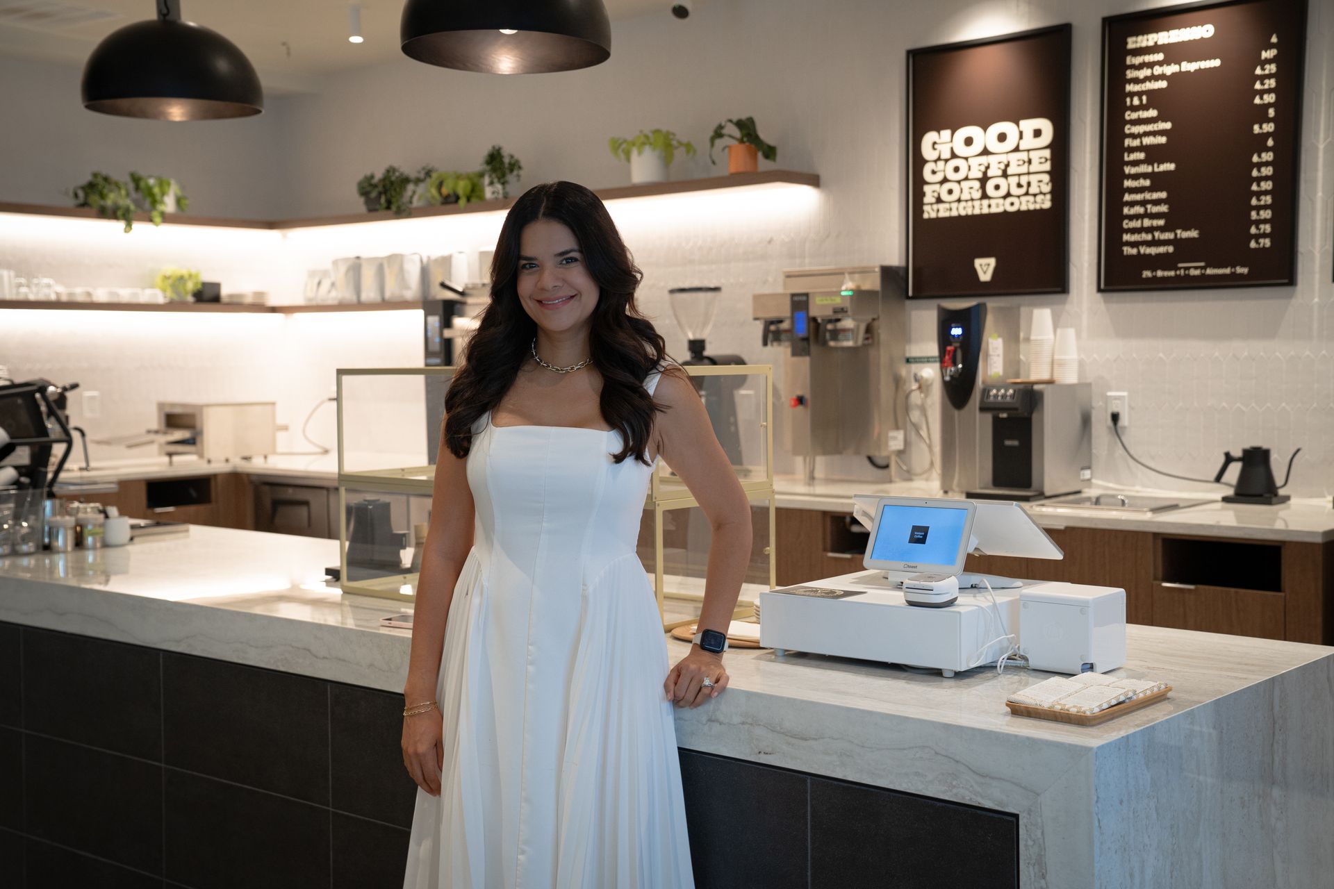 Woman in a white dress standing in a bright café beside the counter