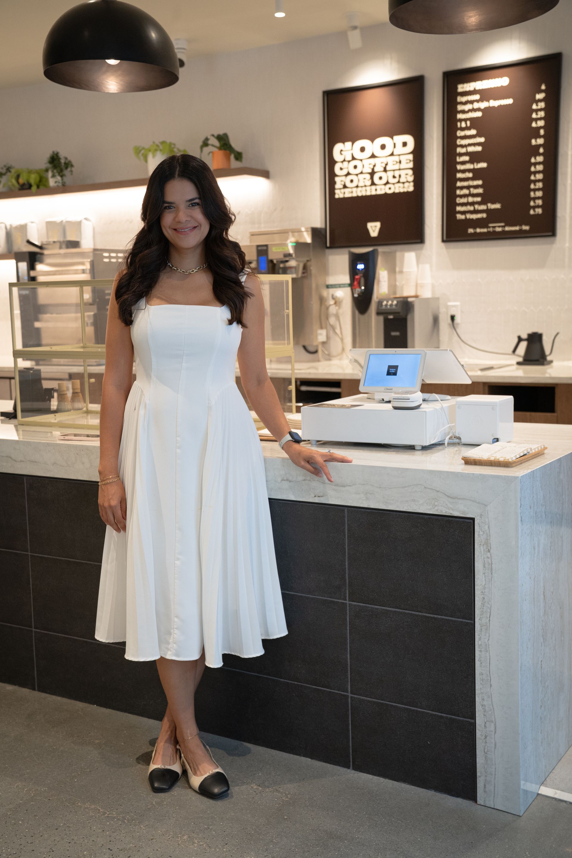 Woman in a white dress standing at a counter in a modern café or dessert shop.