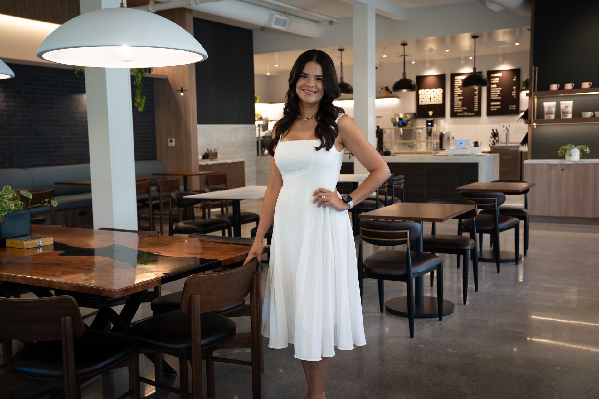 Woman in a white dress standing in a modern restaurant and smiling