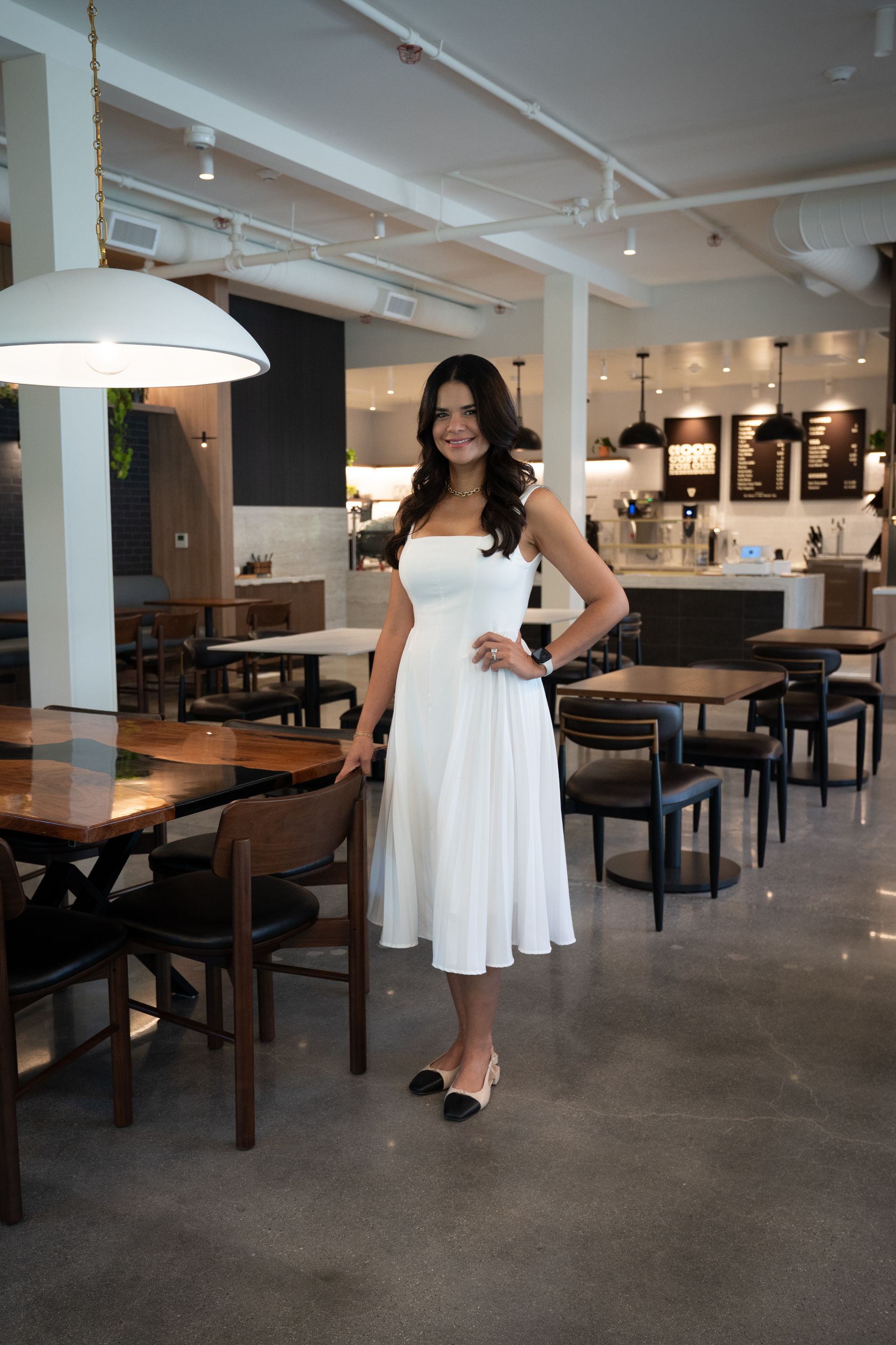 Woman in a white dress standing in a modern café or restaurant interior.