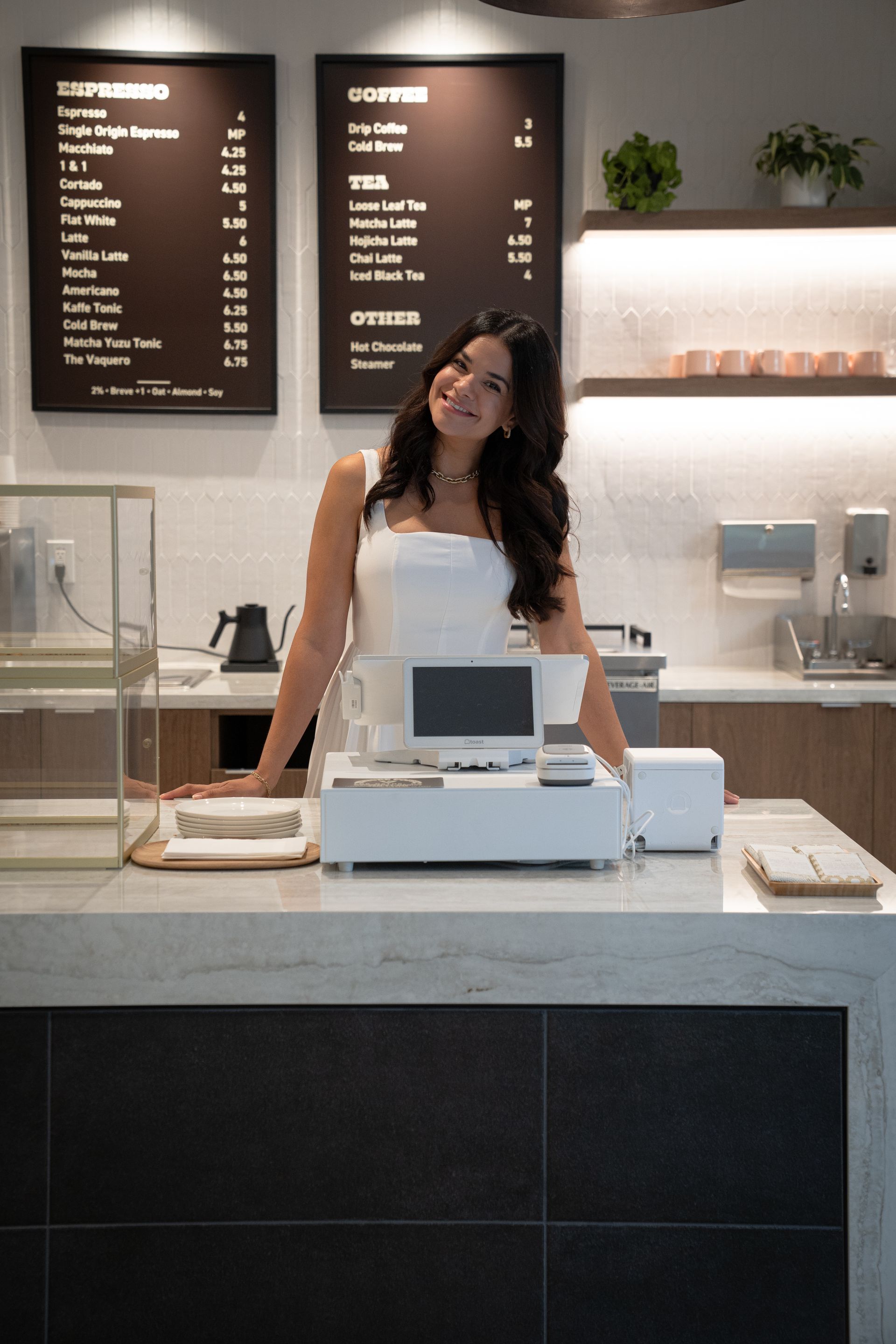 Woman behind café counter with cash register and menu boards in the background