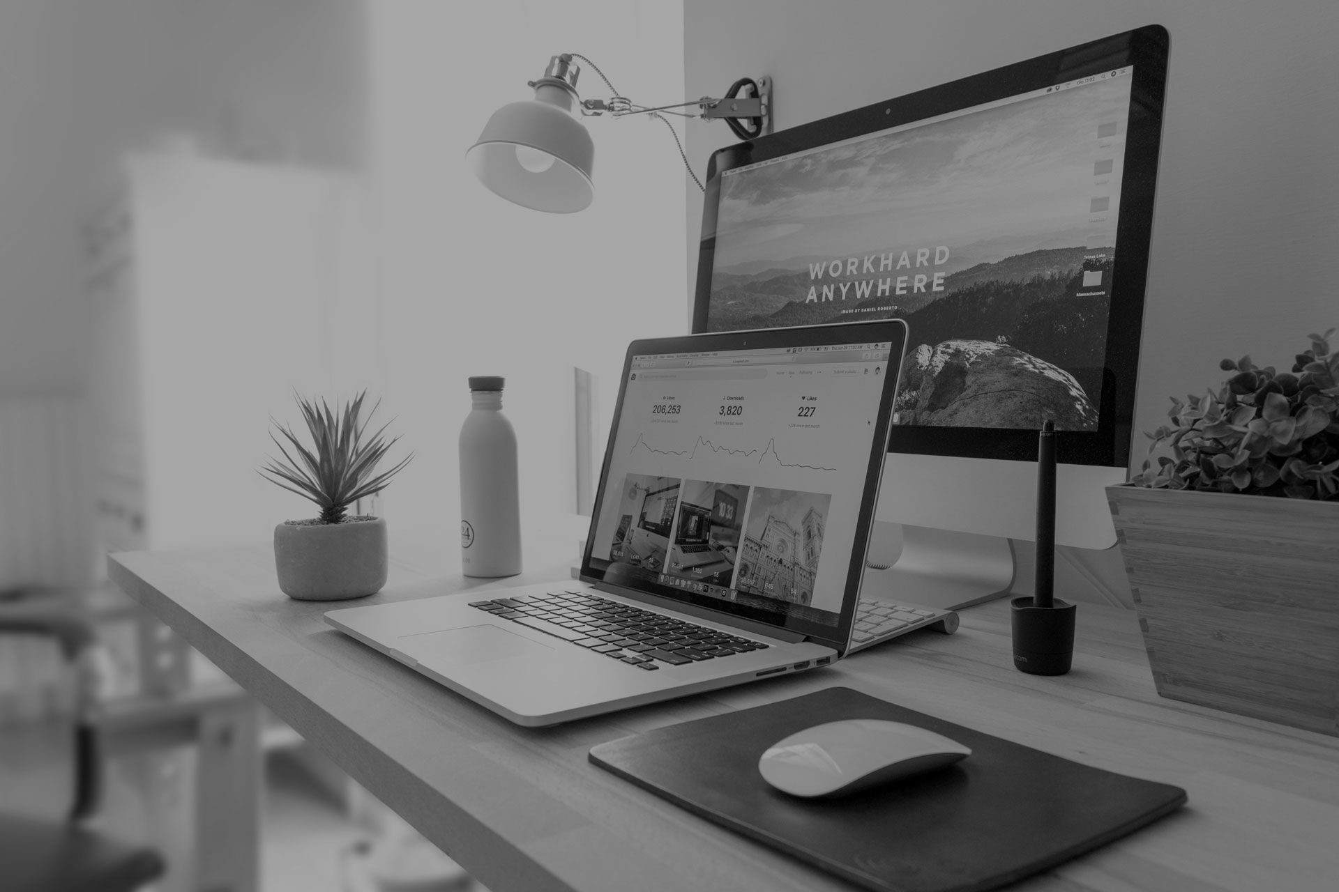 A black and white photo of a desk with a laptop and a computer.