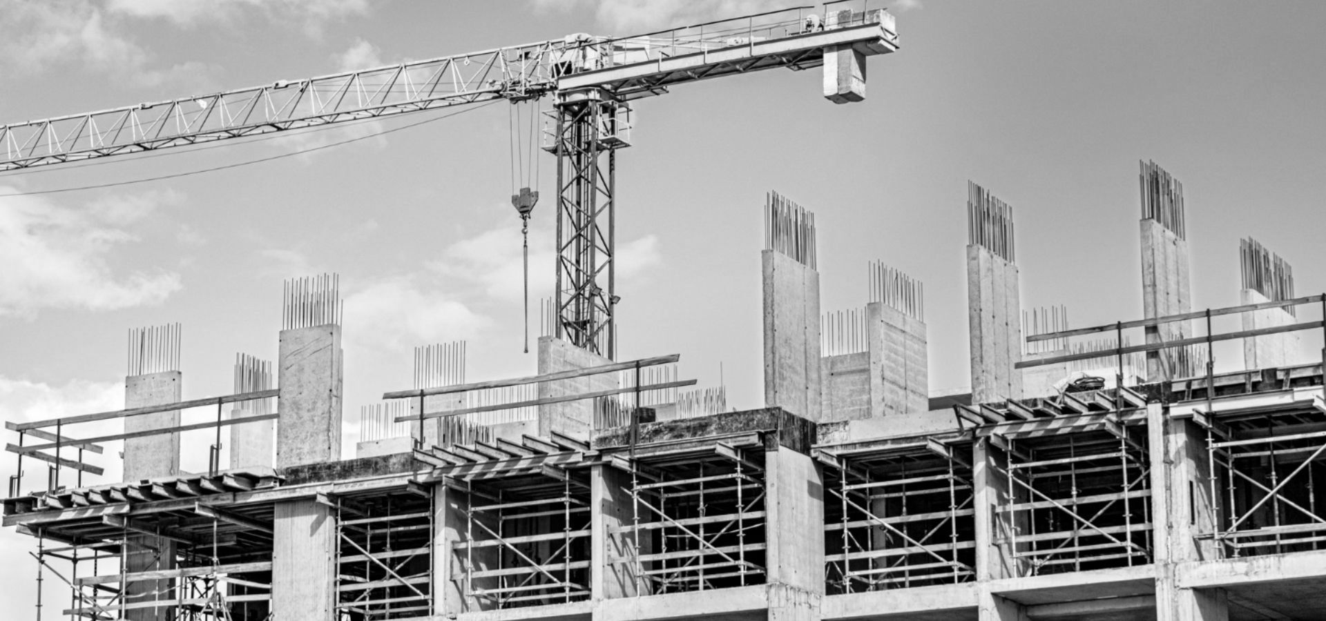 A black and white photo of a building under construction with a crane in the background.