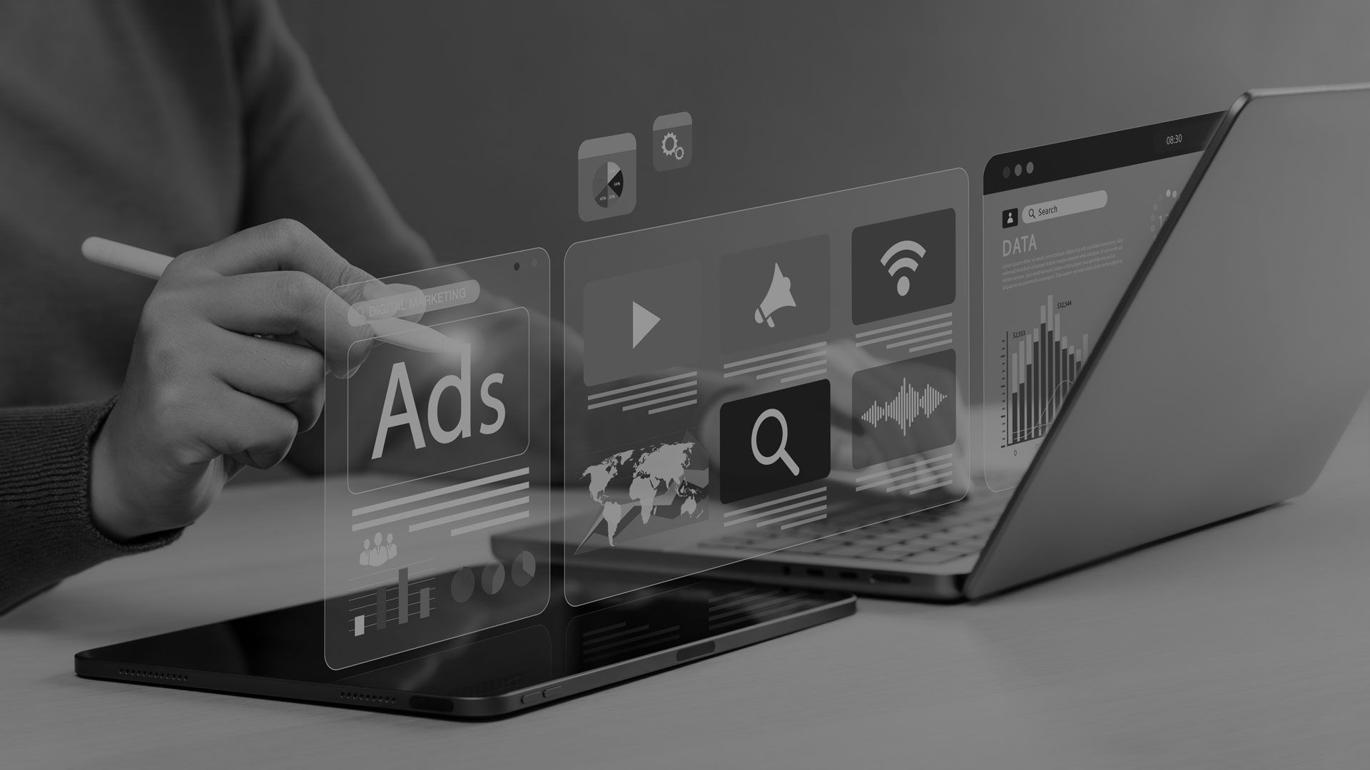 Hands using a laptop with floating digital ad and search icons in a gray workspace