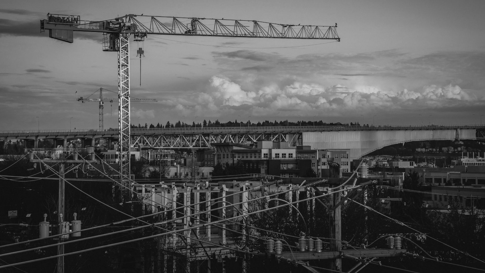A black and white photo of a construction site with a crane in the foreground.