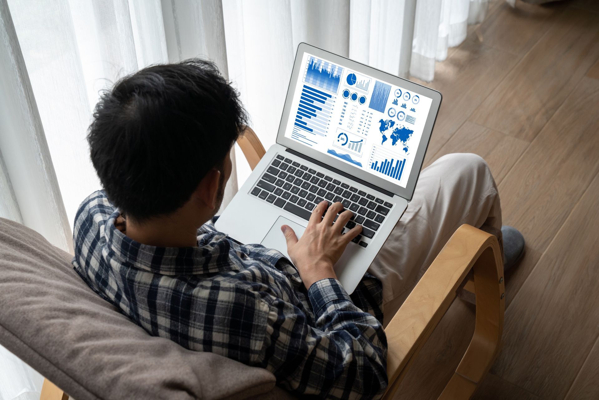Person working on a laptop, displaying charts and graphs while seated in a chair near a window.