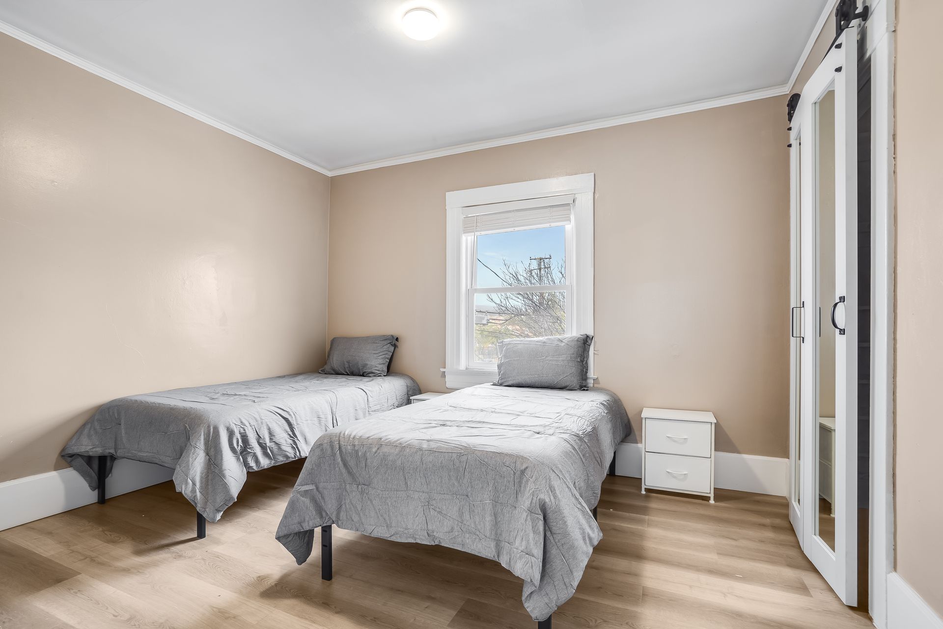 A bedroom with two twin beds, a window, a closet, and neutral-colored walls and floors.