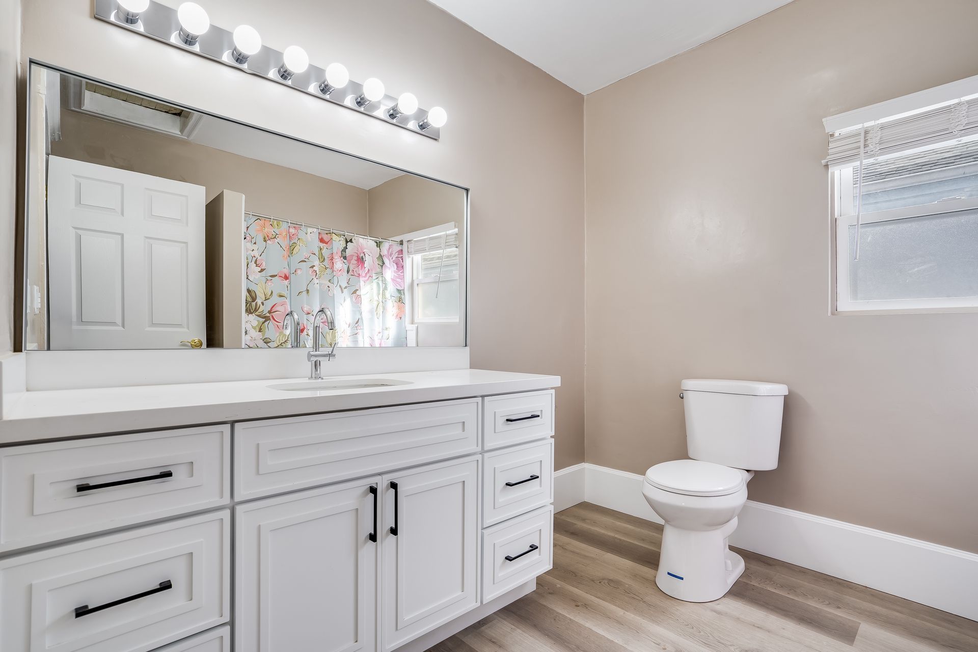 White bathroom with a vanity, toilet, and a window. Neutral walls, wooden floor.