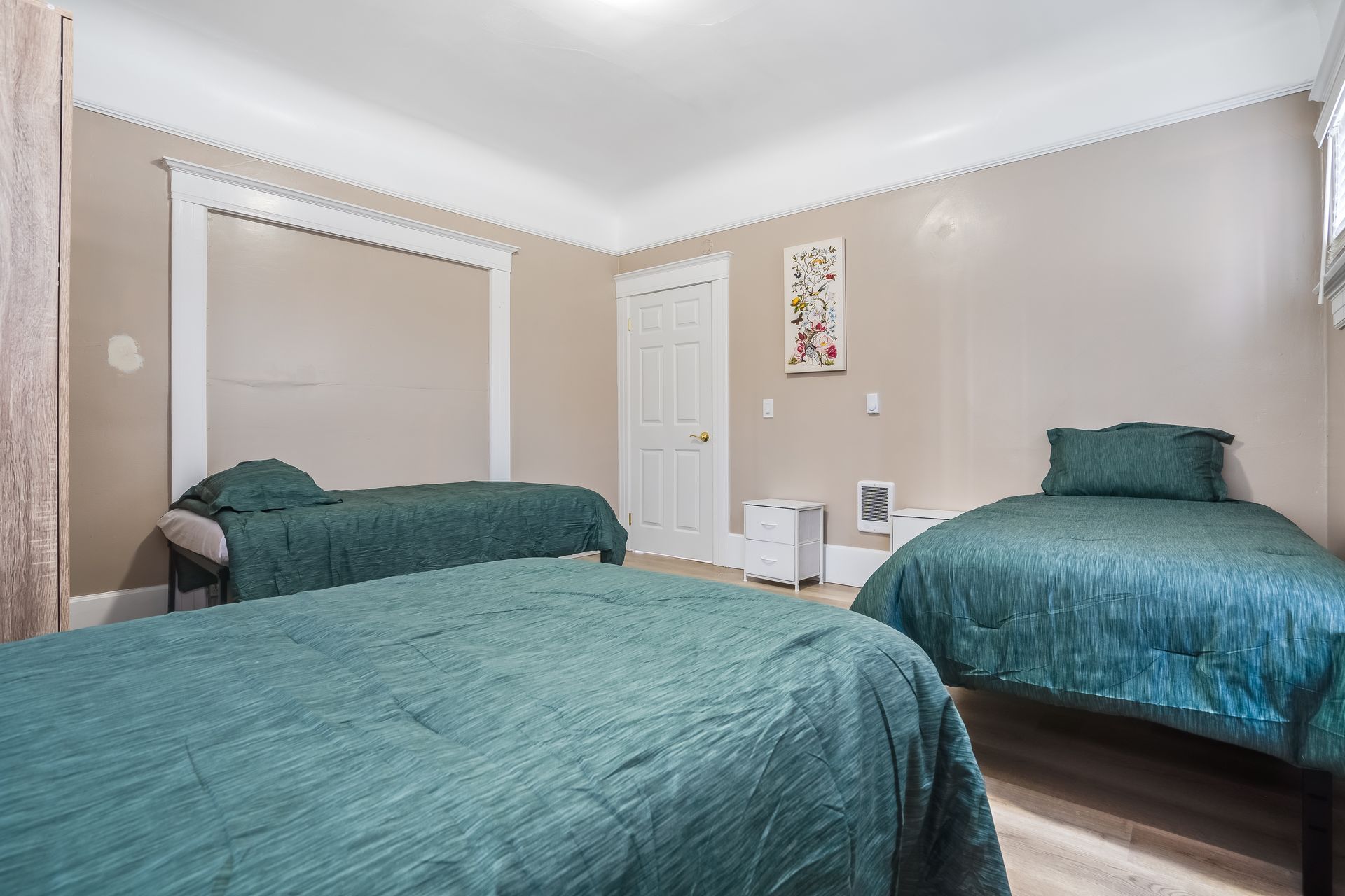 Three beds in a beige bedroom with teal bedding; white door, window, and trim.