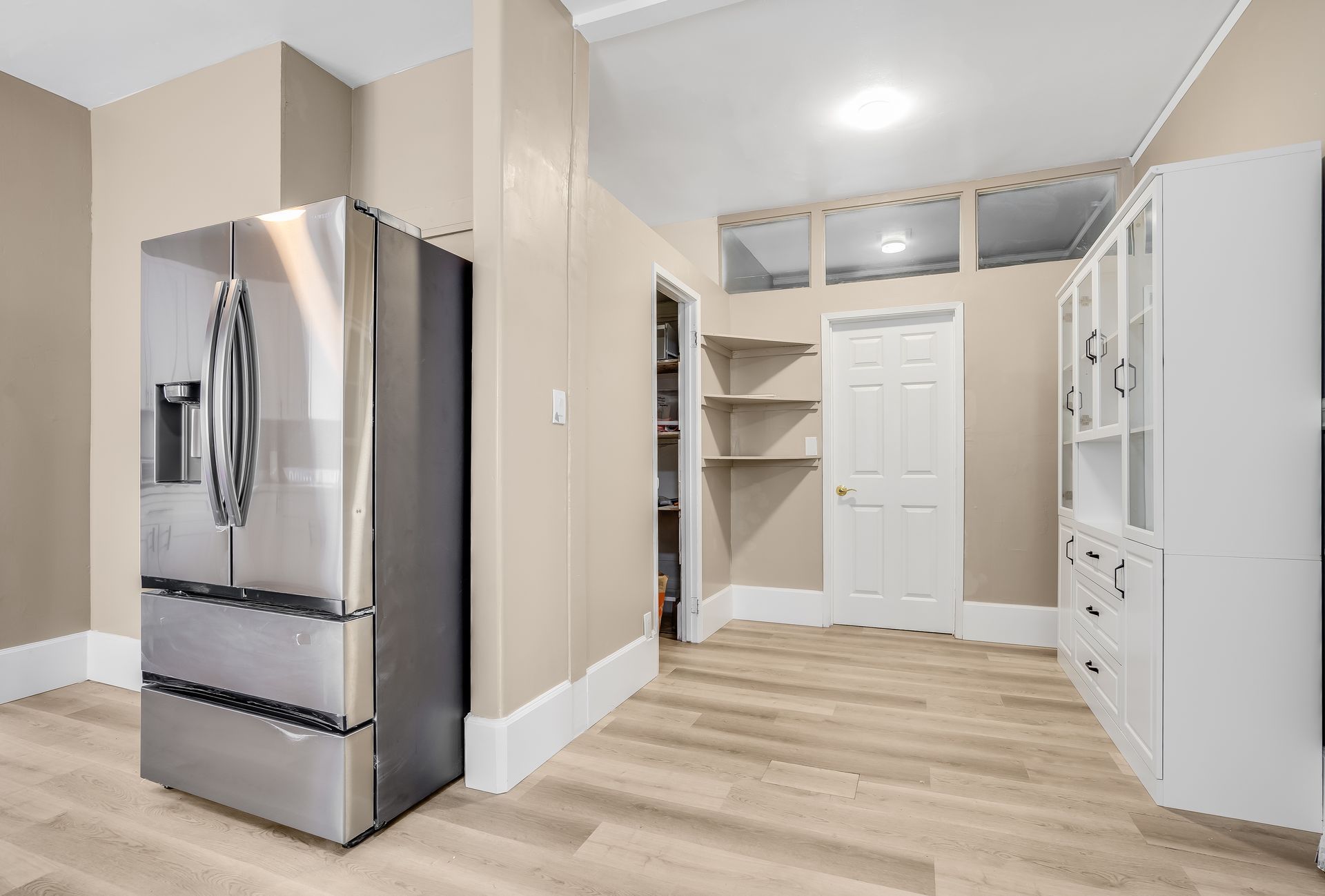 Stainless steel refrigerator next to tan walls, light wood floor, and white pantry.