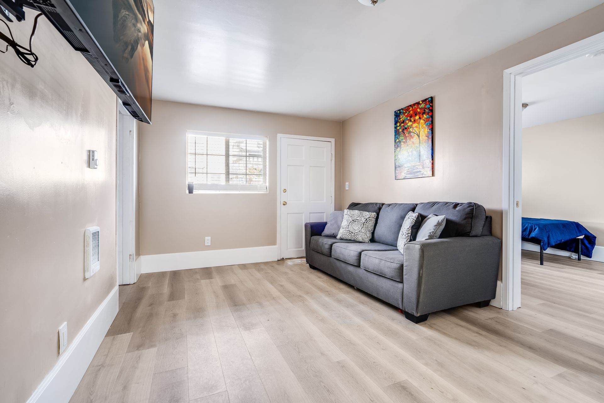 Living room with a gray sofa, artwork, and doorway to bedroom.