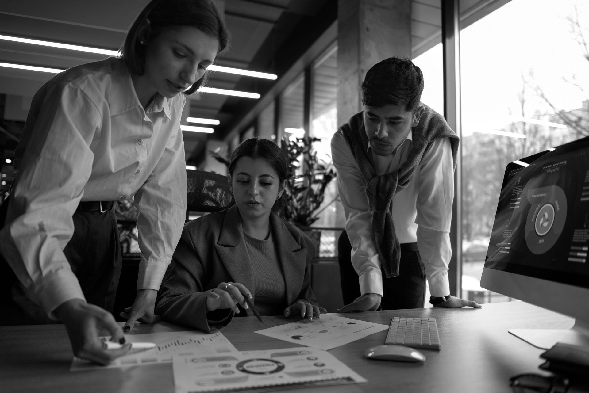 Three colleagues reviewing charts at a desk in a bright office, with a laptop displaying a circular dashboard.