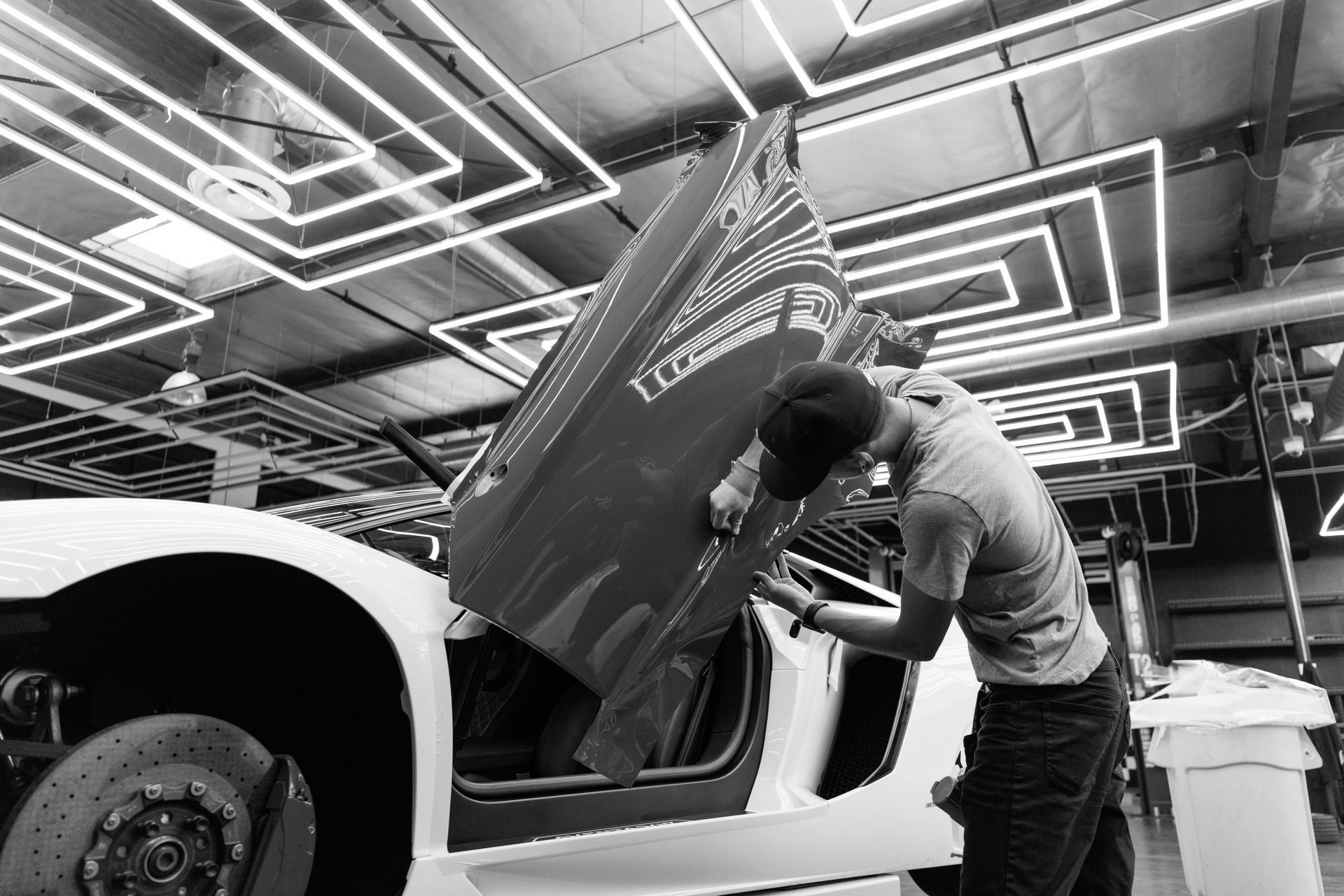 Man working on a white car door, inside a well-lit garage.