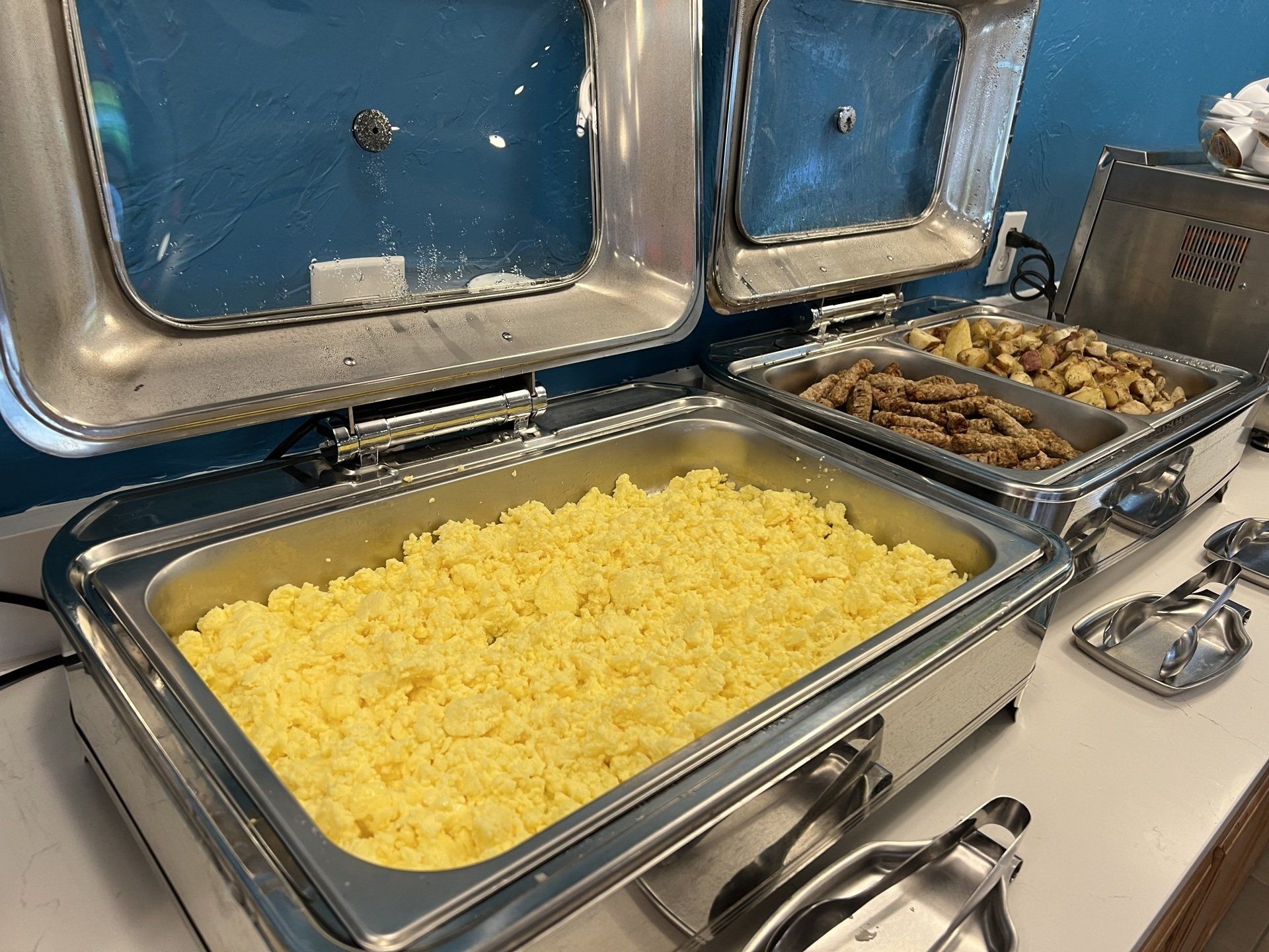 Breakfast buffet with scrambled eggs and potatoes in warming trays.