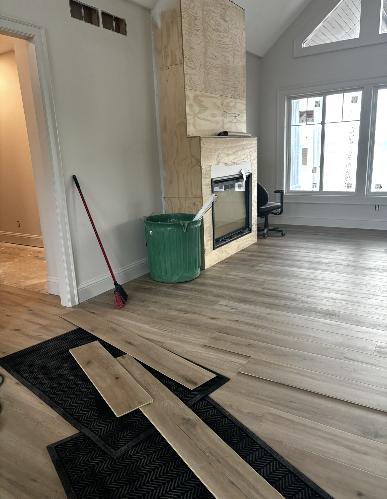 Interior with unfinished flooring, fireplace, and materials; green trash can and broom visible.