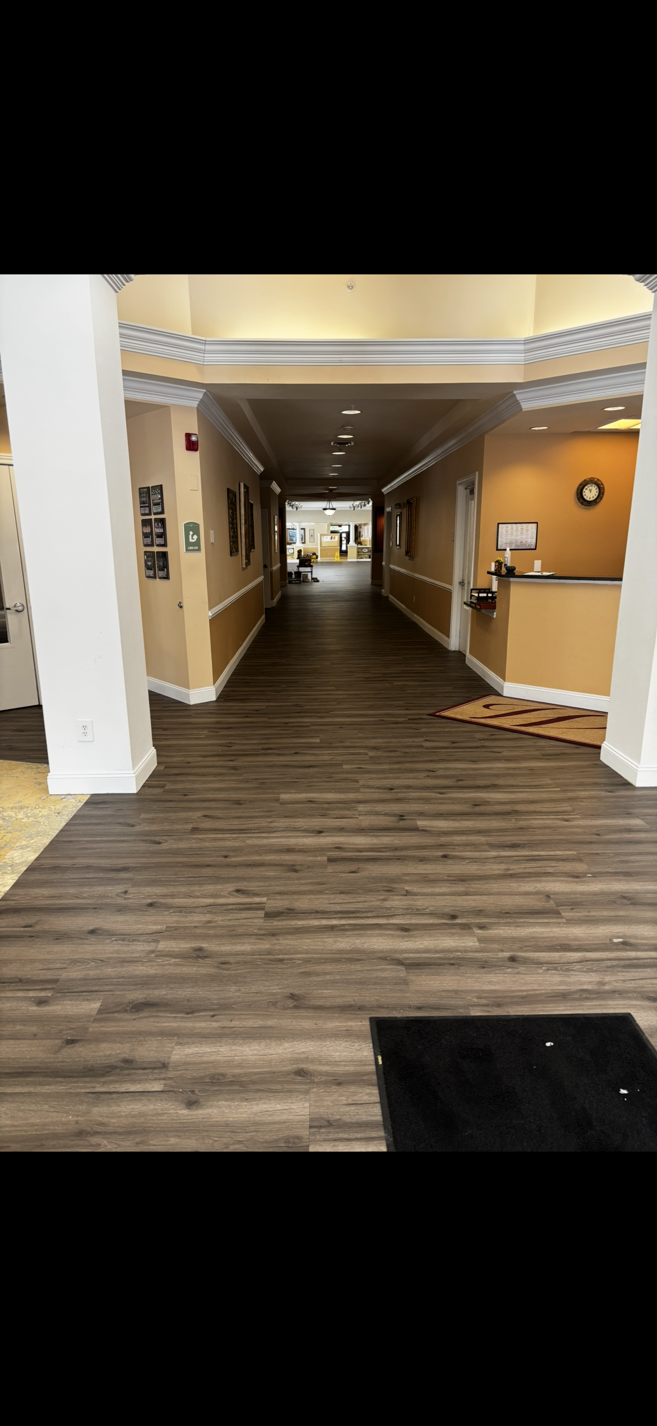 Hallway in a building with wooden flooring and tan walls. A reception desk is at the end.