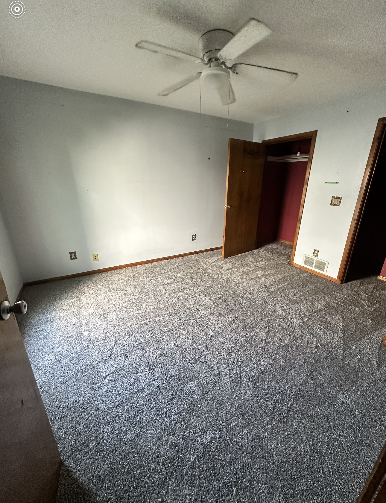 Bedroom interior with gray speckled carpet, white walls, closet, and ceiling fan.