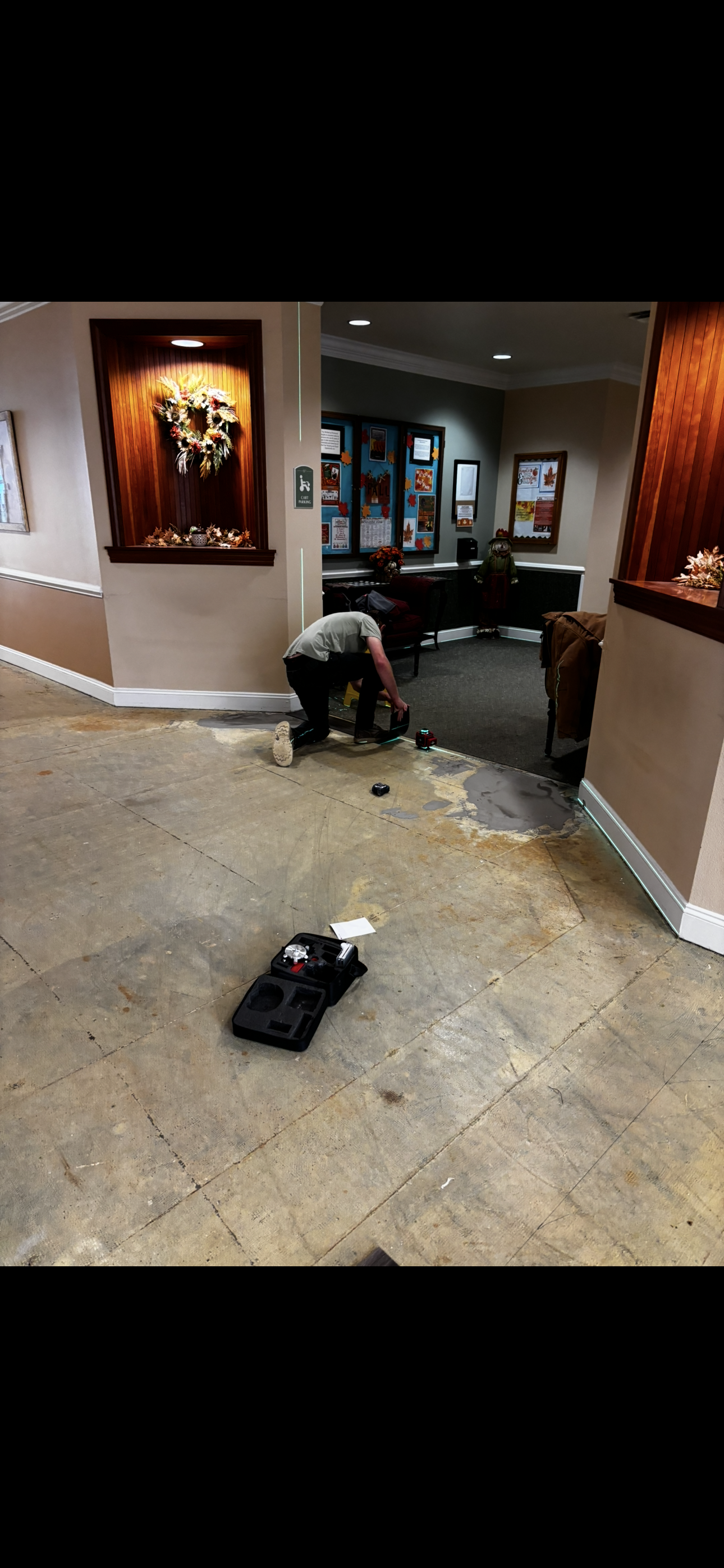 Person kneeling on floor removing flooring in a hallway. Tools and debris are visible.