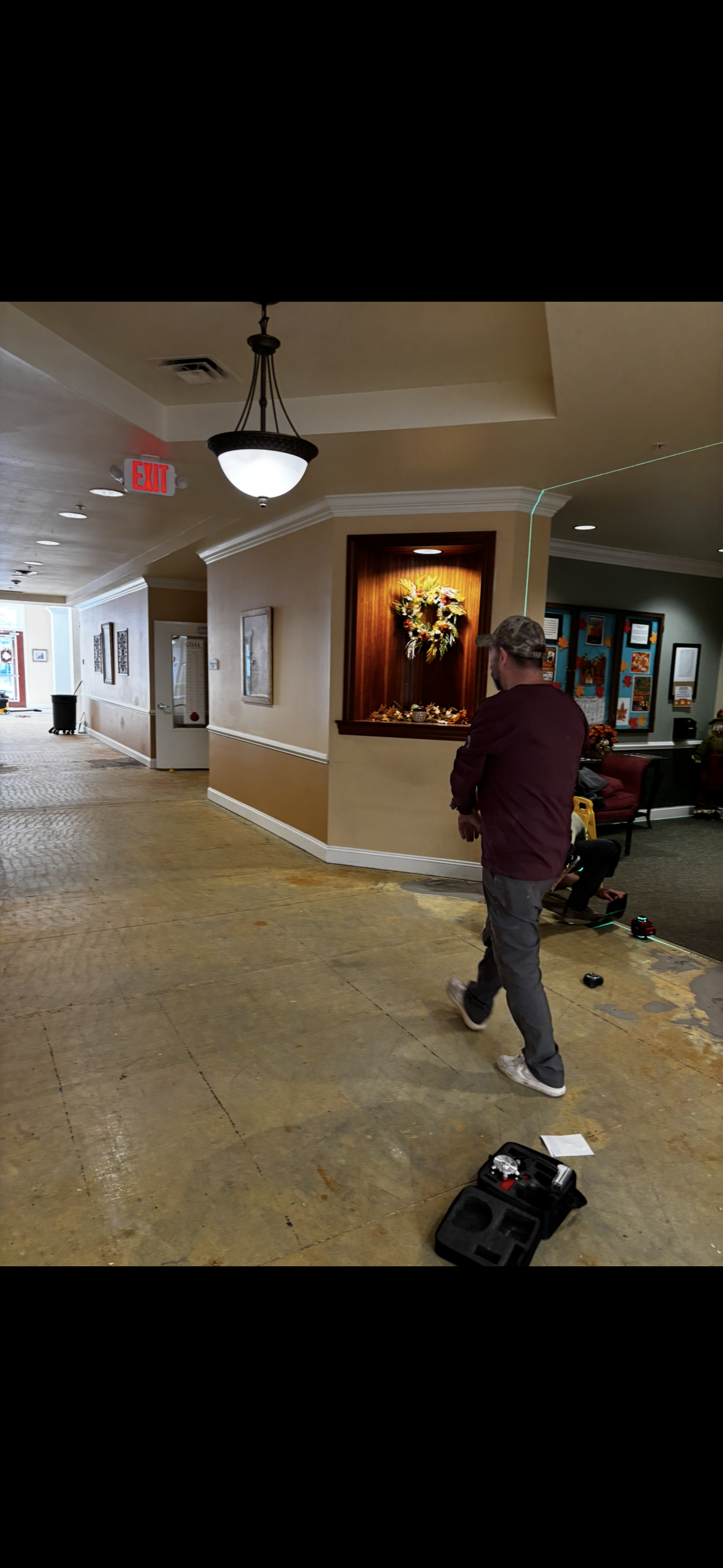 A man walks down a hallway with a recessed display case. The floor is stripped of flooring.