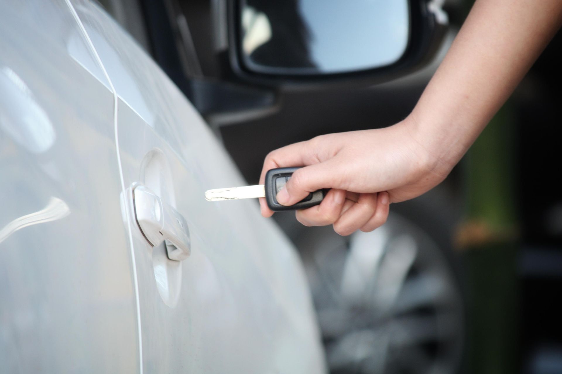 Hand inserting a car key into a white car door lock
