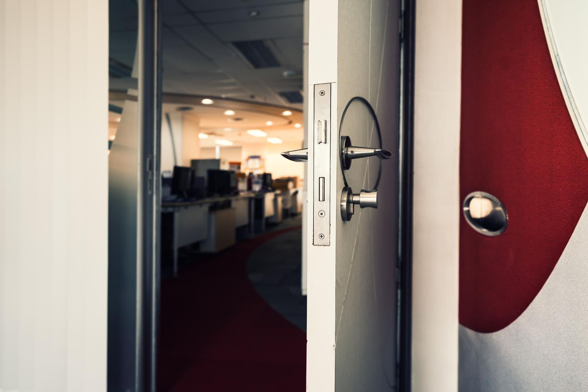 Open office doorway with red carpet and white walls, showing desks and warm lighting inside