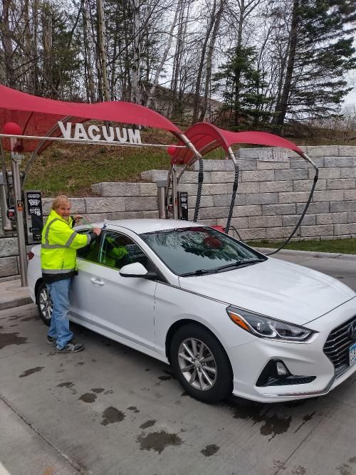 Worker in a neon jacket washing a white car at a vacuum car wash under red canopies