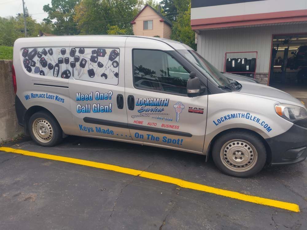 White service van with blue lettering parked by a yellow curb in a driveway near a house.