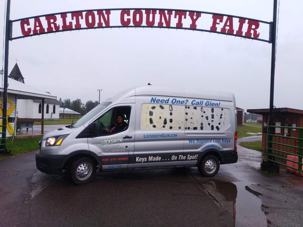 White van under the Carlton County Fair sign on a rainy day, advertising a local business.