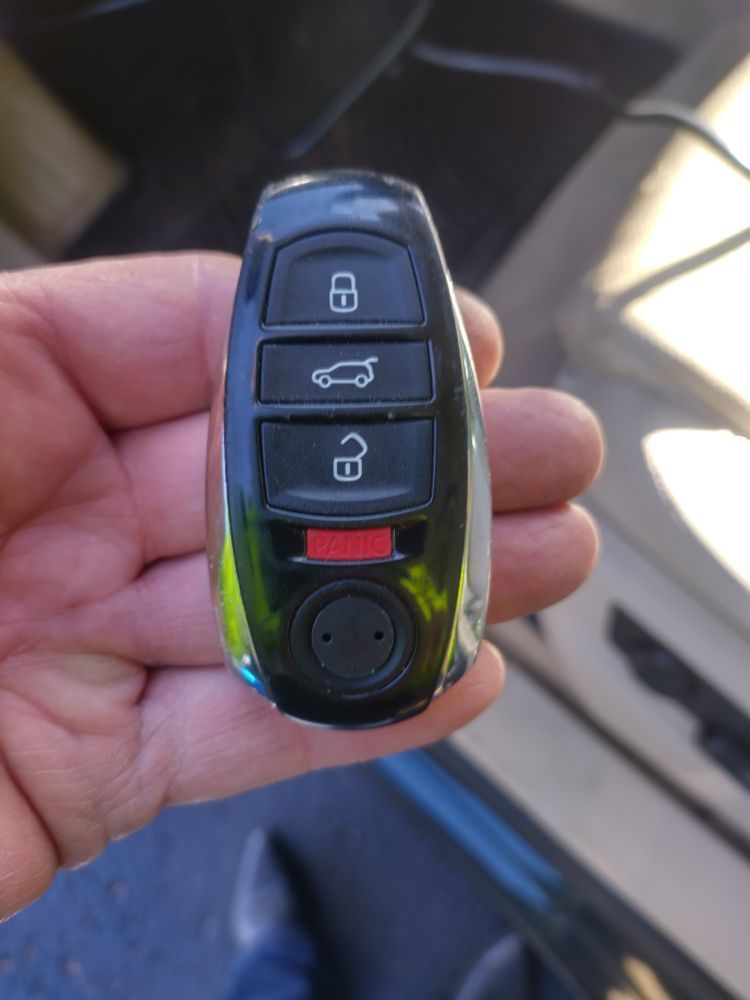 Hand holding a black car key fob with lock, trunk, unlock buttons and a red panic button